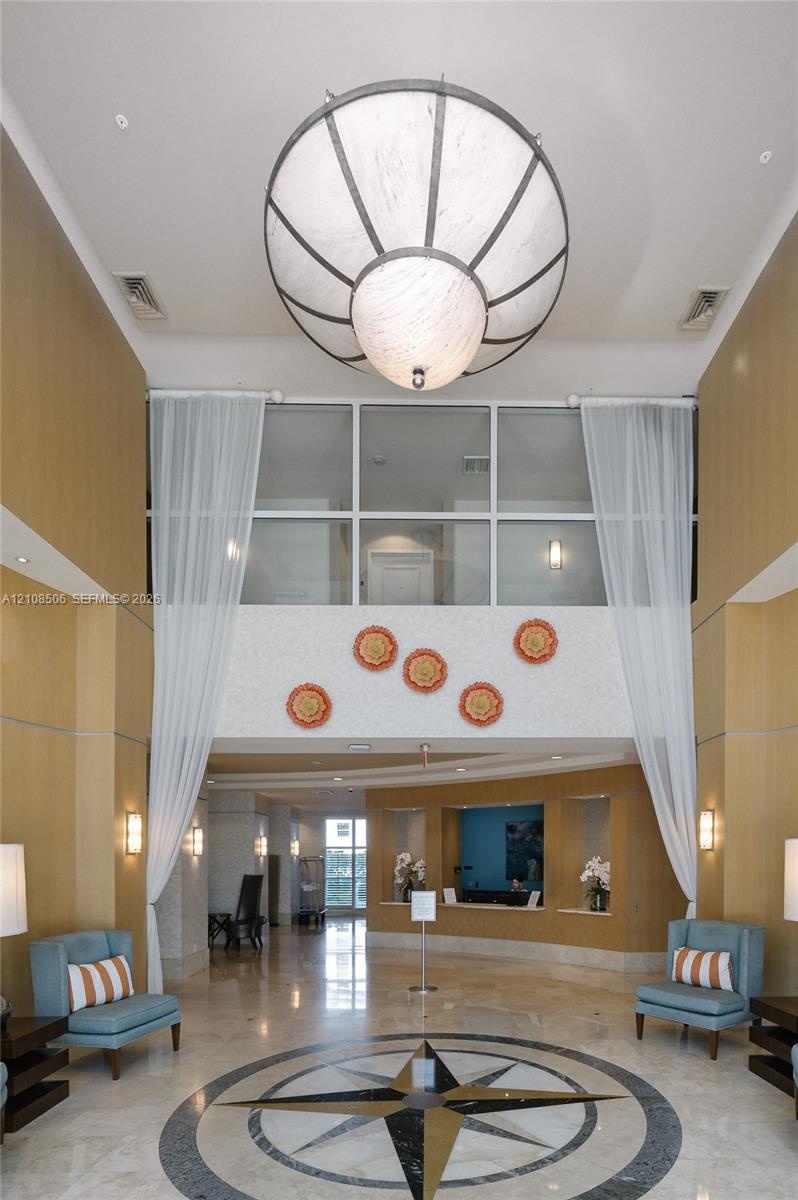 Grand entrance lobby featuring double-height ceilings, a large spherical pendant light, stone flooring with an inlaid compass rose medallion, wood-pan