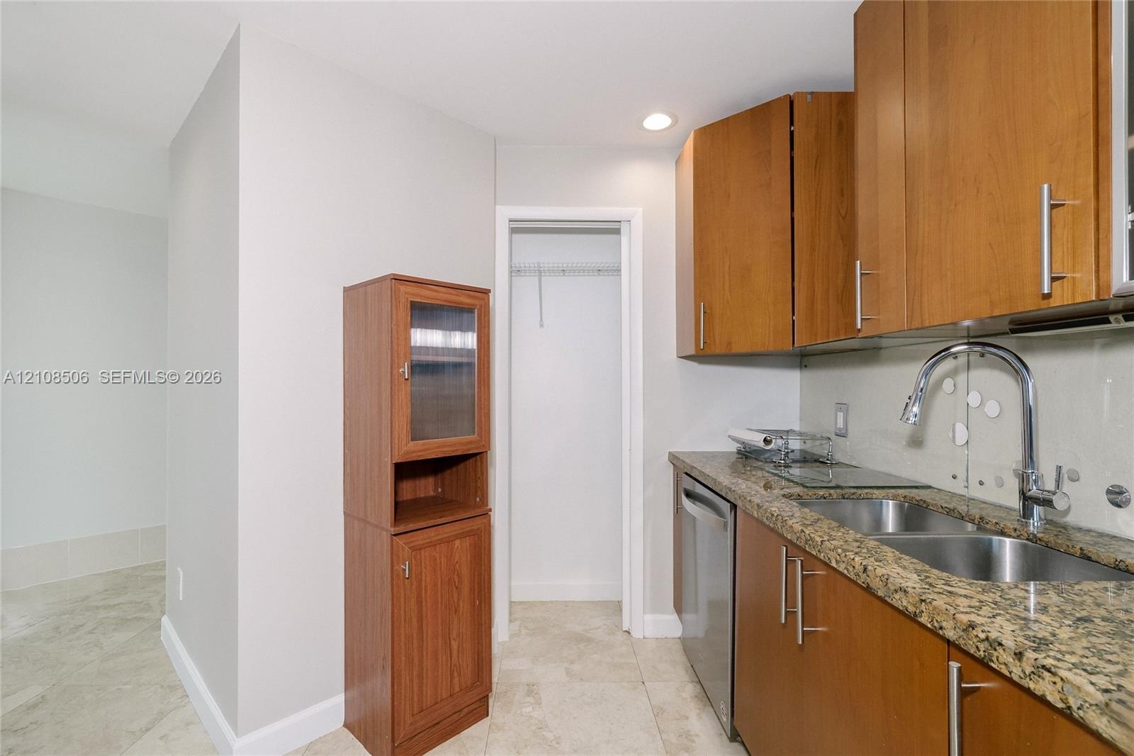 Kitchen area featuring wood cabinetry, stone countertops, double-basin undermount sink with a gooseneck faucet, stainless steel dishwasher, and tile f