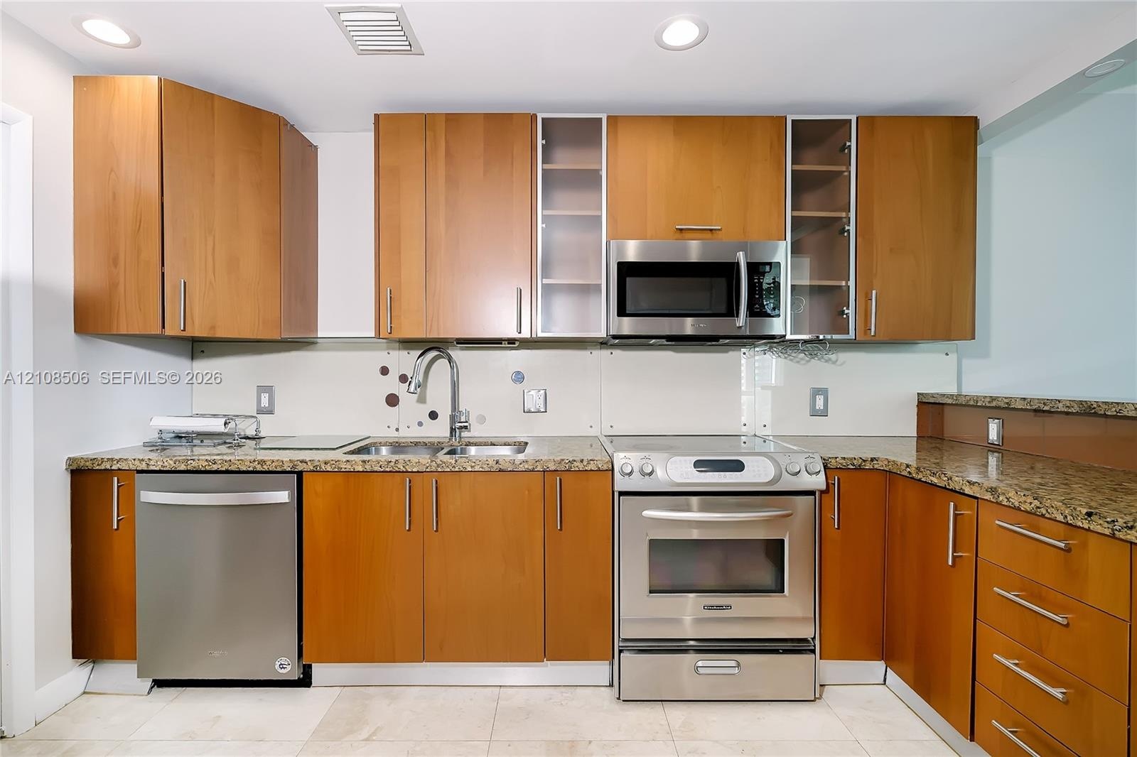 Kitchen featuring wood-finish cabinetry, stone-surface countertops, stainless steel appliances, glass-front upper cabinet doors, and recessed ceiling 