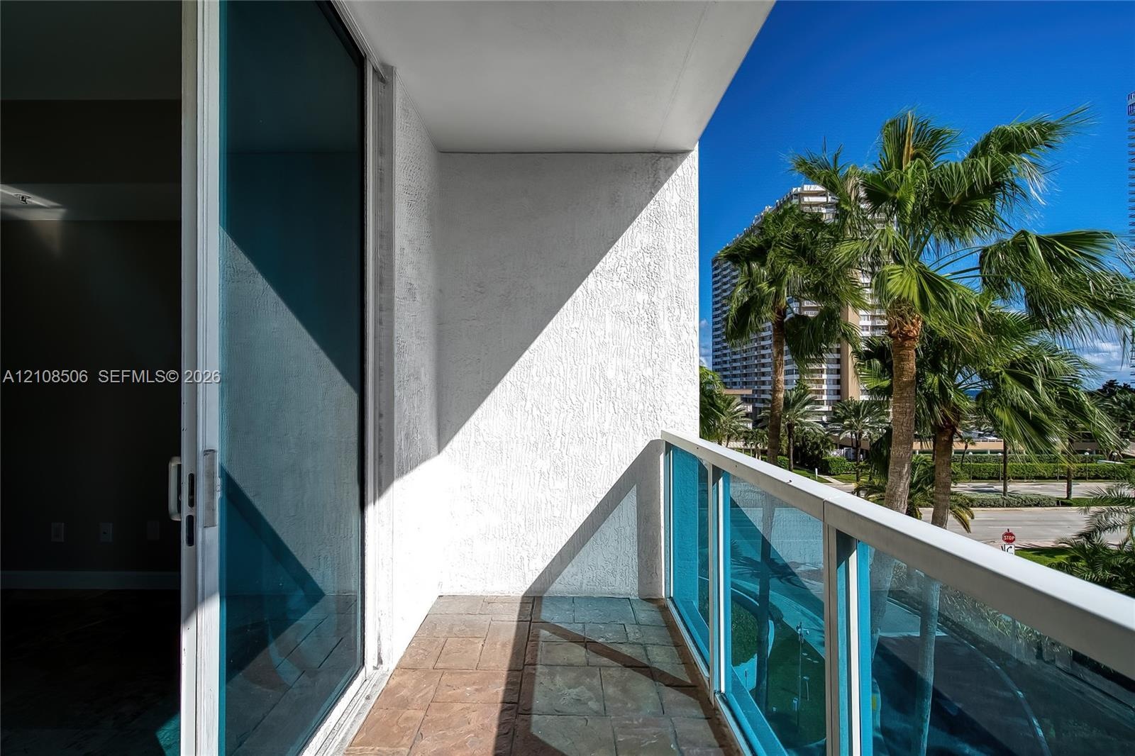 Private balcony featuring textured stucco walls, tiled flooring, and a glass-paneled railing with a metal frame