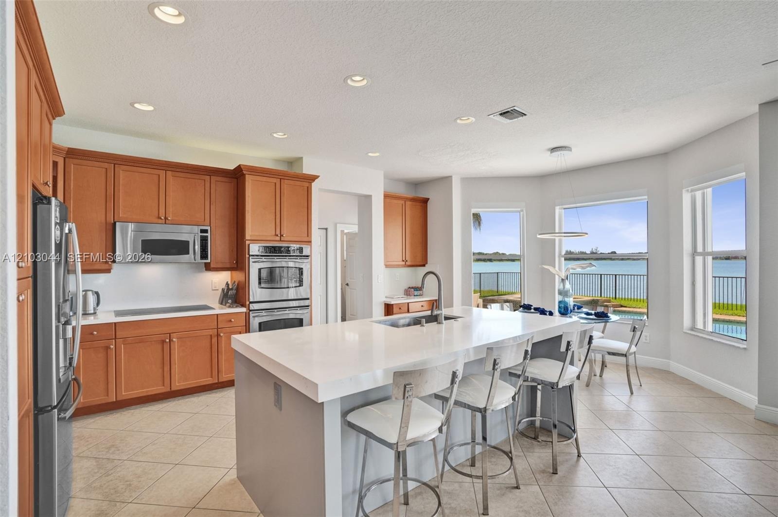 Kitchen featuring shaker-style cabinetry, quartz countertops, a central island with an integrated sink, built-in stainless steel double ovens, and wat