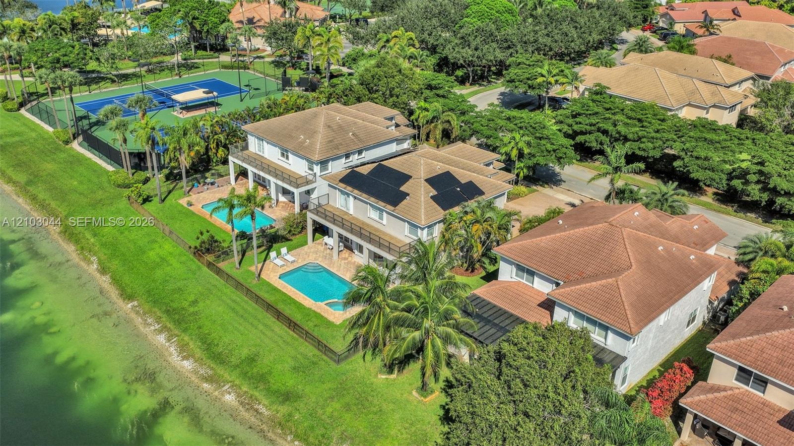 Two-story residence featuring a private swimming pool, solar panel array, tiled roof, and balconies with metal railings