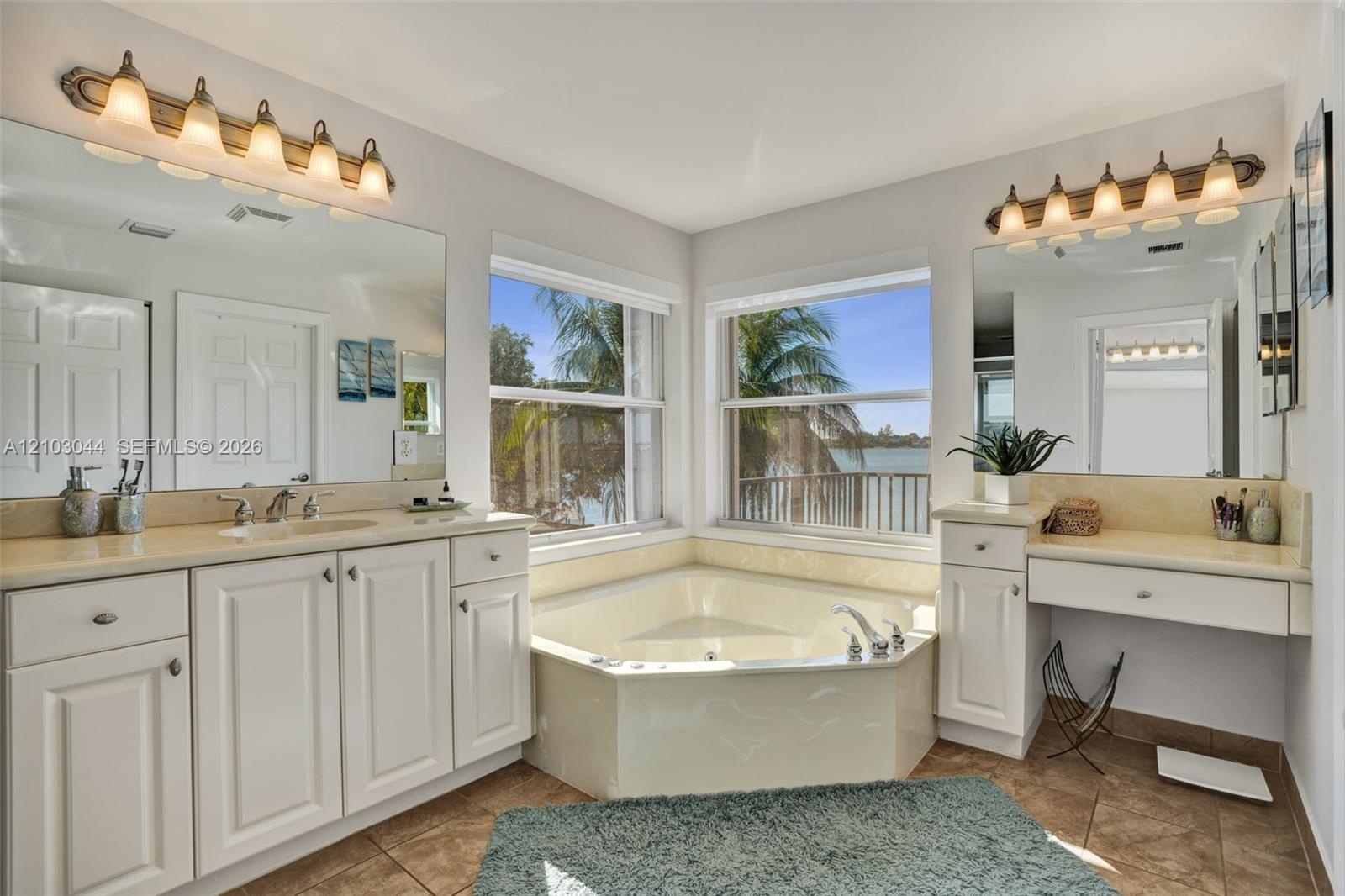 Bathroom featuring a corner soaking tub, dual vanity with stone countertops, integrated makeup vanity, and two large wall-mounted mirrors