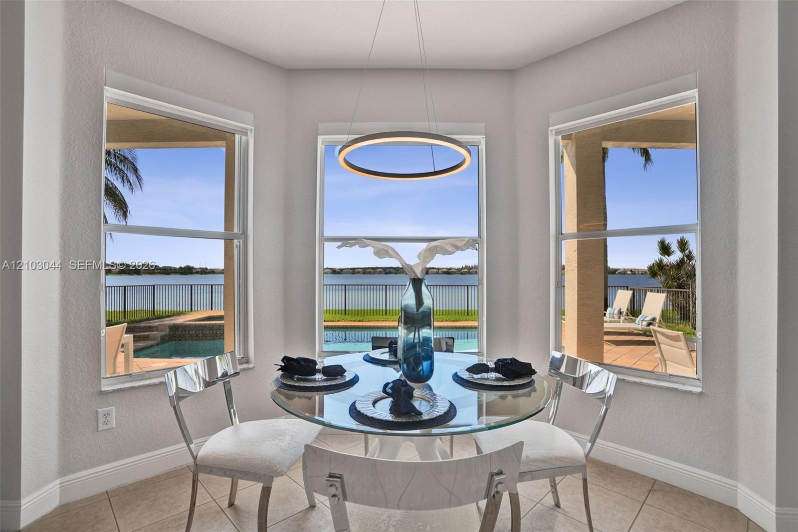 Bay window featuring large-format tile flooring, a circular LED pendant light, and triple-pane windows showcasing the pool, patio, and lakefront