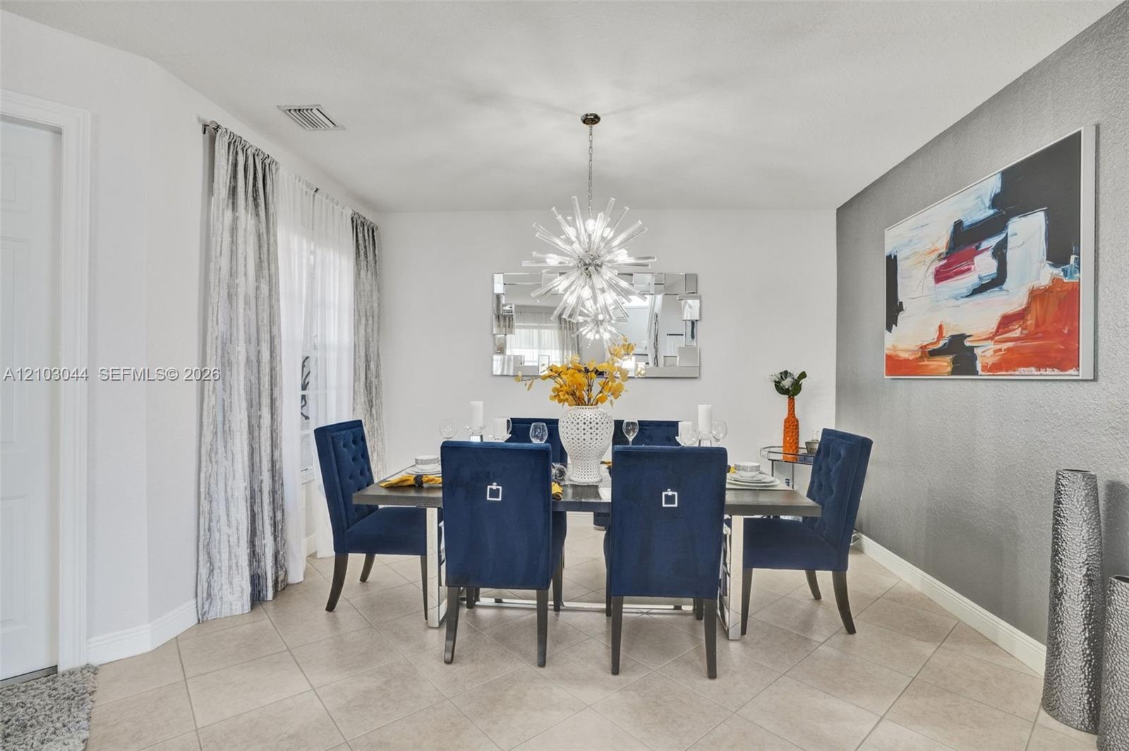 Dining space featuring oversized ceramic tile flooring, a neutral color palette with a grey accent wall, and a multi-spoke sunburst-style overhead lig