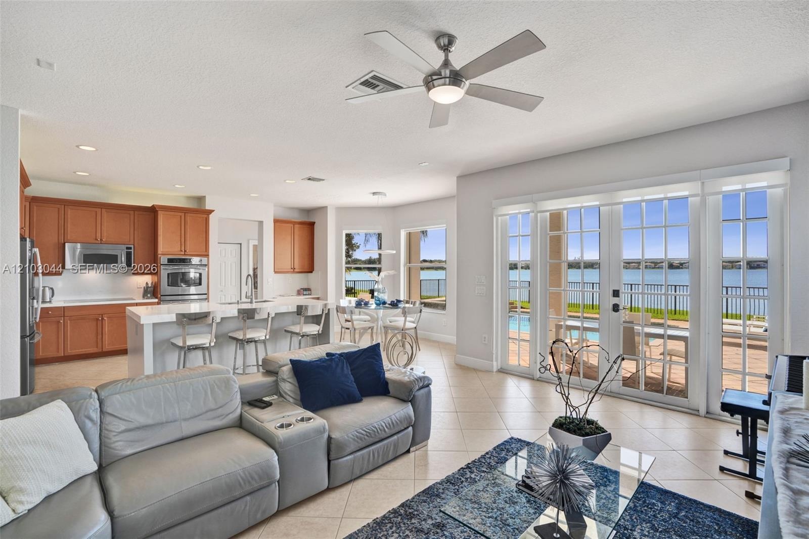 Open-concept living space featuring wood-finish cabinetry, a waterfall-edge center island with a built-in sink, recessed lighting, a modern ceiling fa