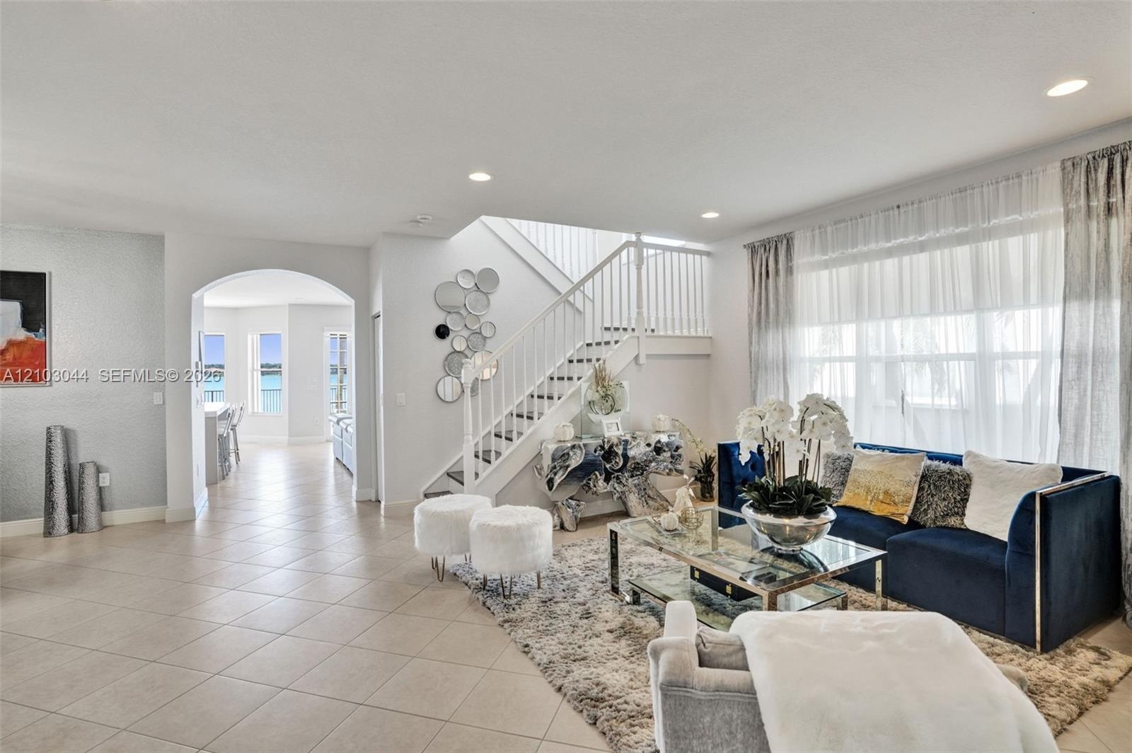 Open-concept floor plan featuring tile flooring, a prominent staircase with white balusters, an arched architectural entryway, and large windows with 