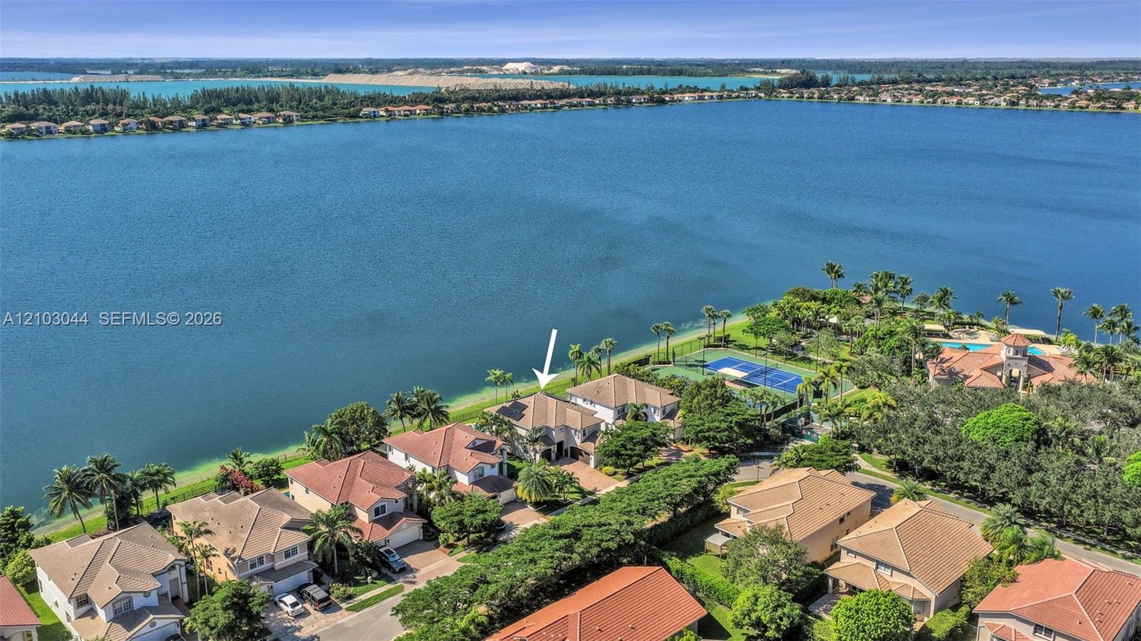 Aerial perspective of waterfront property featuring extensive shoreline access, tile roof construction, and proximity to community-maintained tennis c