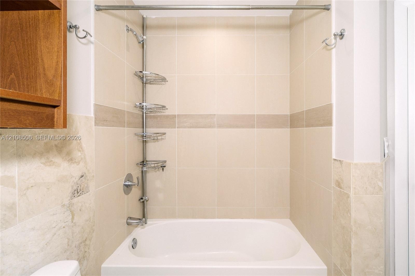Shower area featuring floor-to-ceiling neutral ceramic tiling, an integrated stone-finish accent band, a built-in recessed tub, chrome plumbing fixtur
