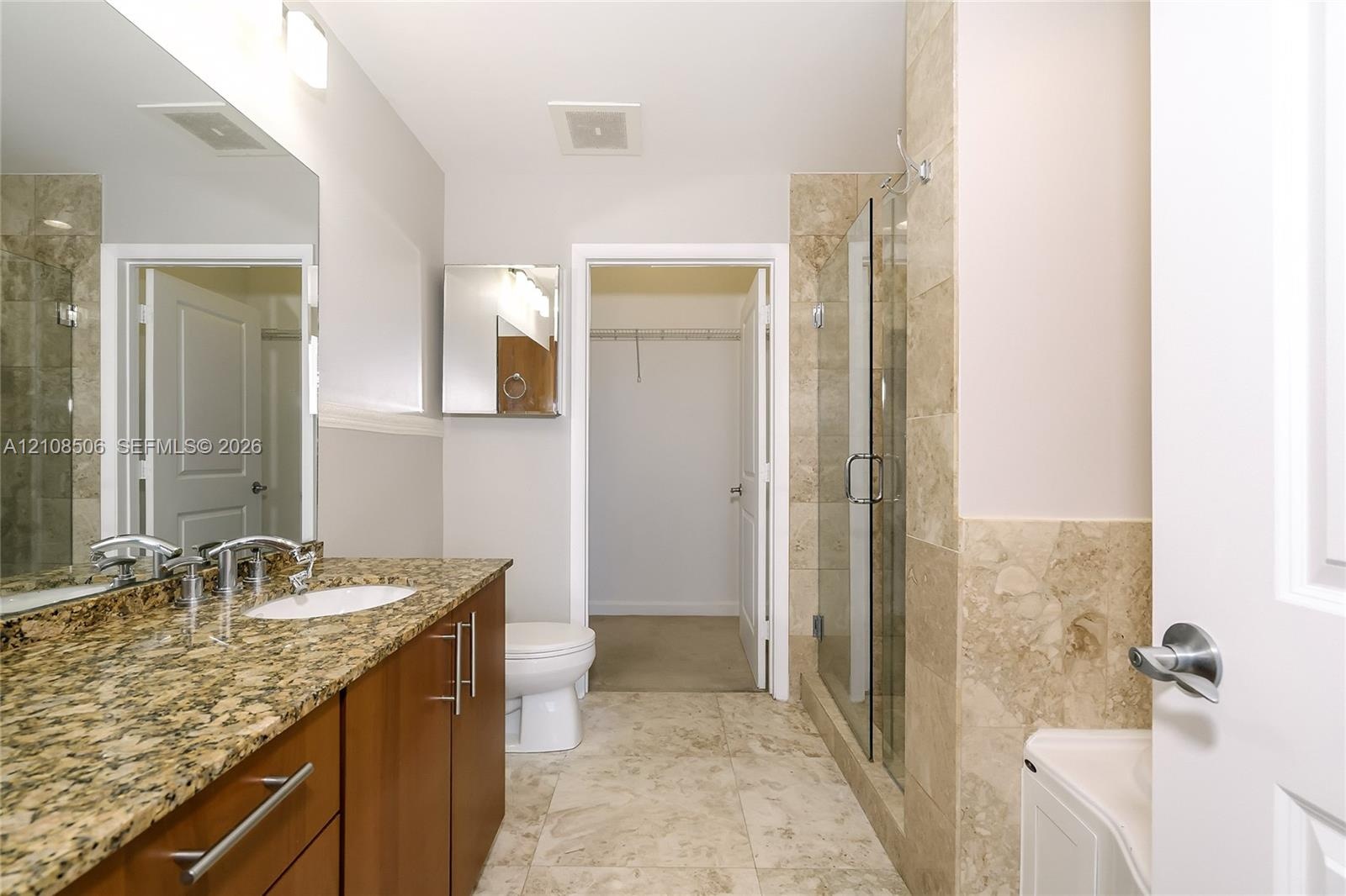 Bathroom featuring a vanity with stone-finish countertop, undermount sink, shower with glass enclosure and stone-finish tile surround, and tile floori
