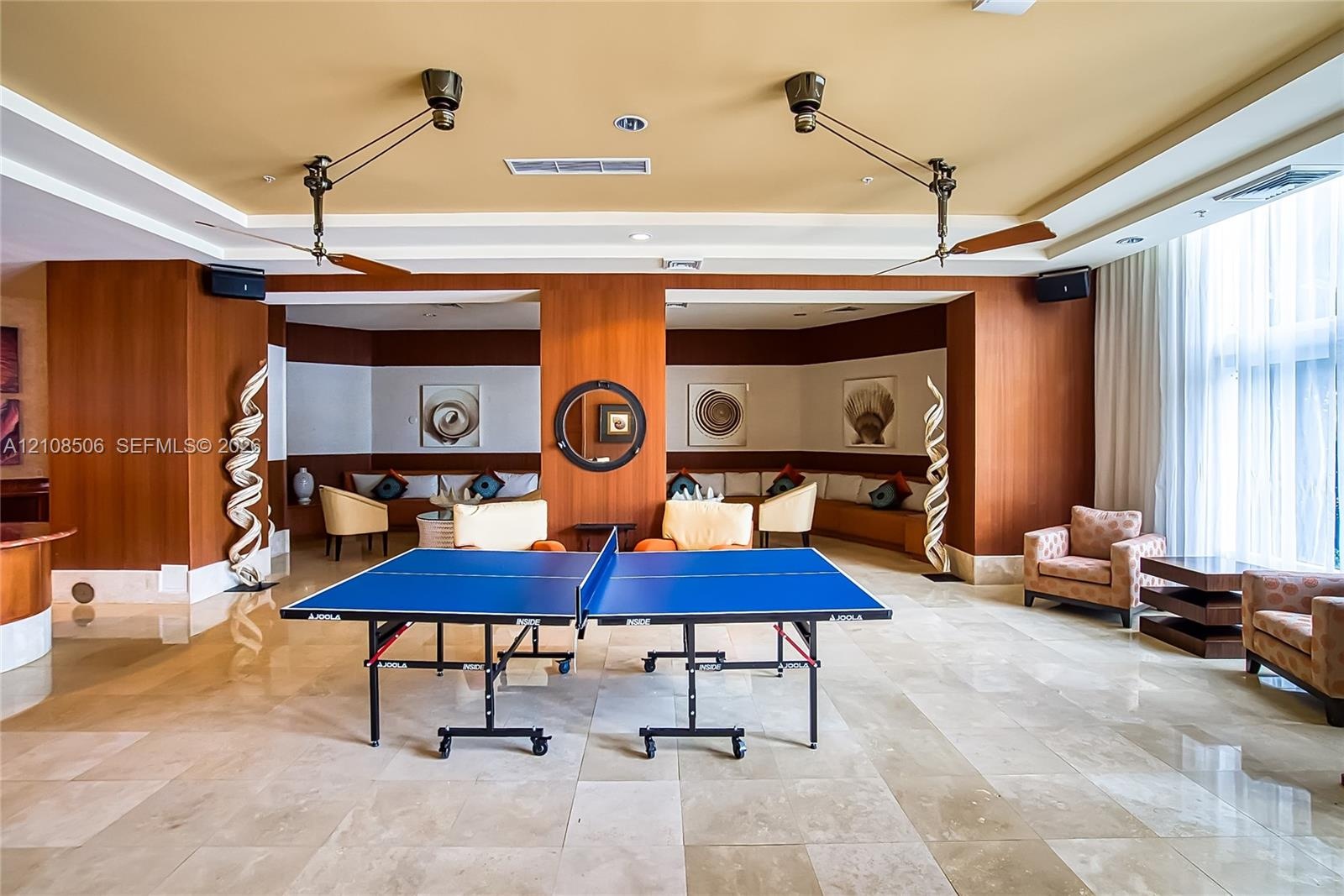 Open-concept common space featuring polished stone flooring, custom wood-panel wall treatments, integrated tiered ceiling lighting, and dual industria