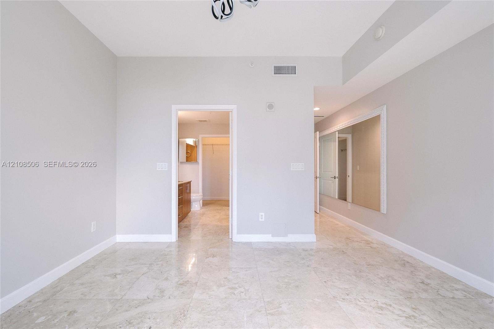 Interior room featuring neutral-toned stone-finish flooring, a large wall-mounted mirror, and a geometric flush-mount light fixture