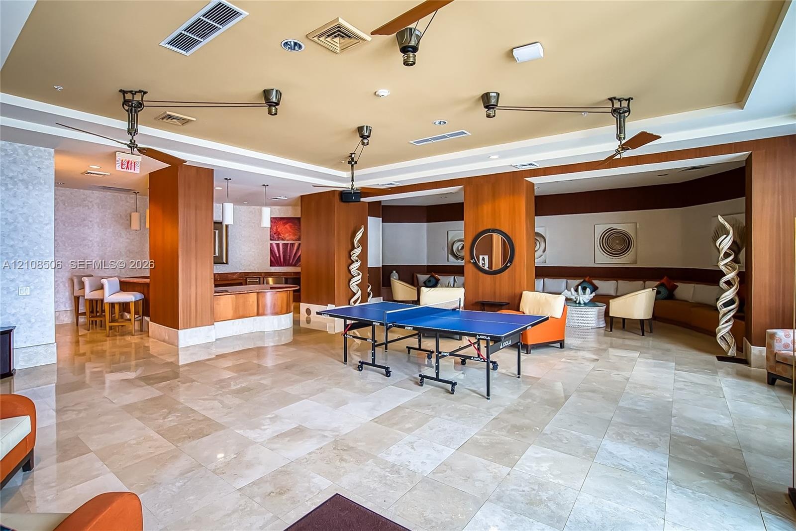 Large common area featuring natural stone tile flooring, wood-paneled columns, built-in bar with stone countertop, recessed lighting, and dual ceiling