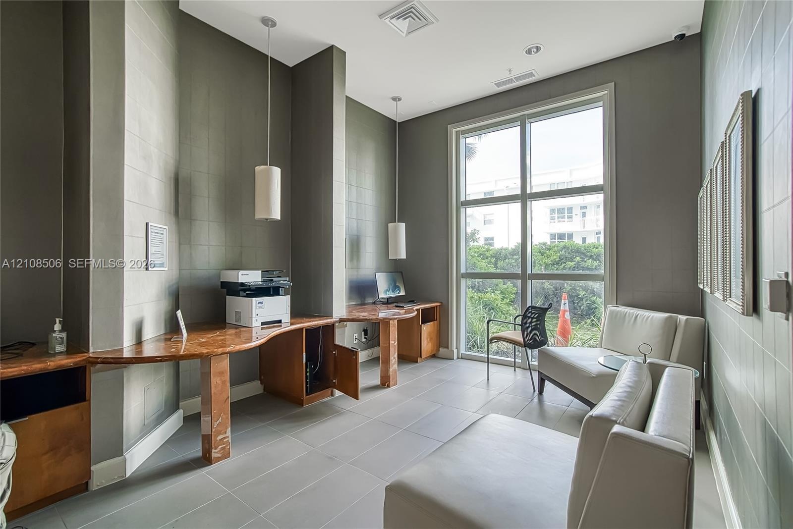 Built-in stone-top desk with integrated wood cabinetry, floor-to-ceiling multi-pane window, large-format tile flooring, and two modern pendant light f