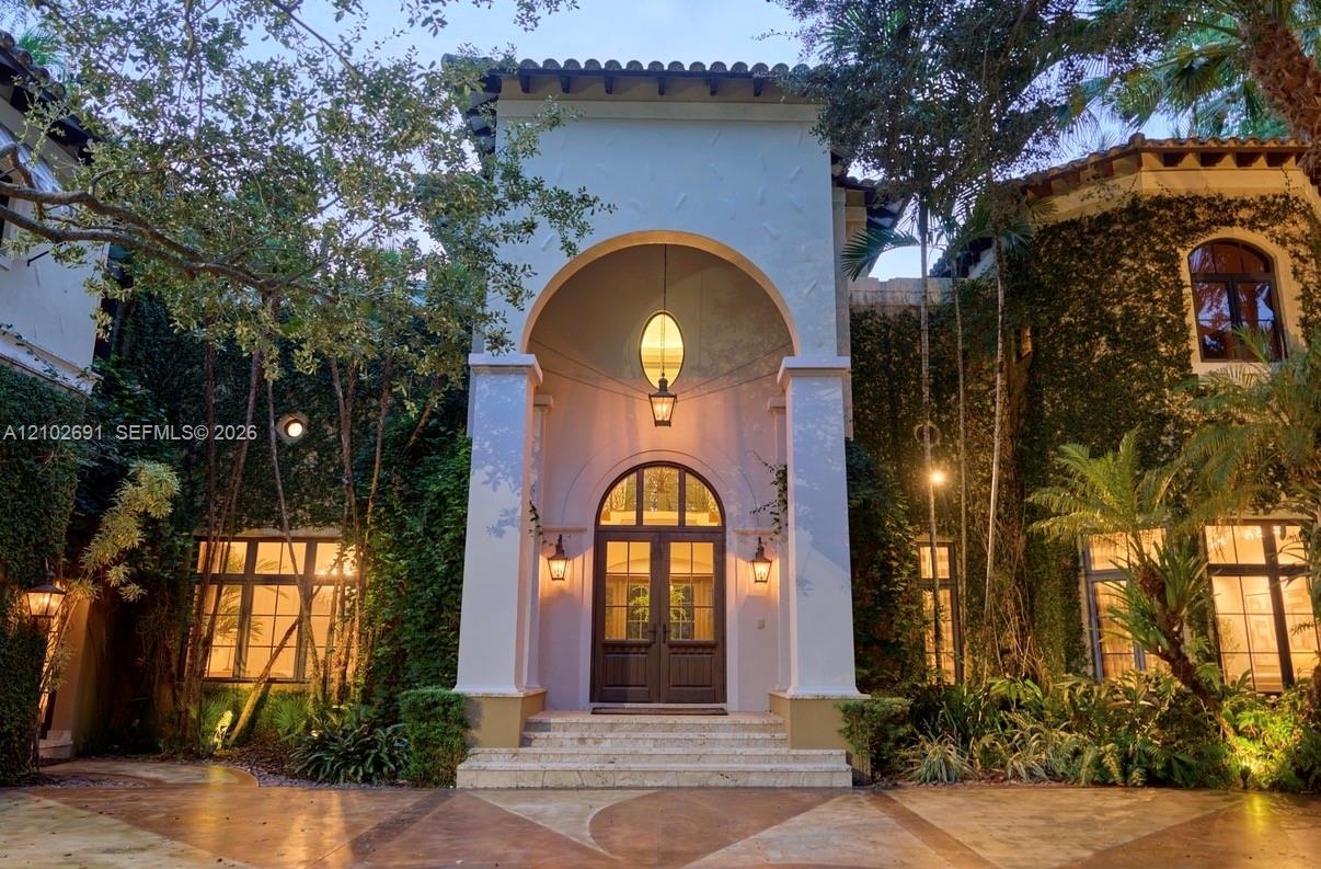 Mediterranean-inspired exterior featuring a grand arched entryway, stucco facade, decorative iron-caged pendant lighting, and stone steps leading to d
