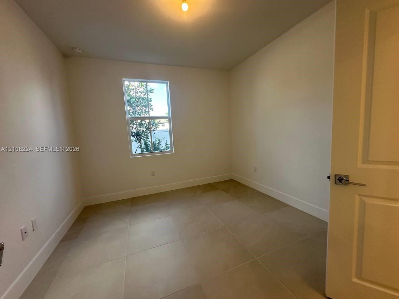 Neutral-toned large-format tile flooring, single-hung window, white interior walls, and a multi-panel door with a satin-finish lever handle