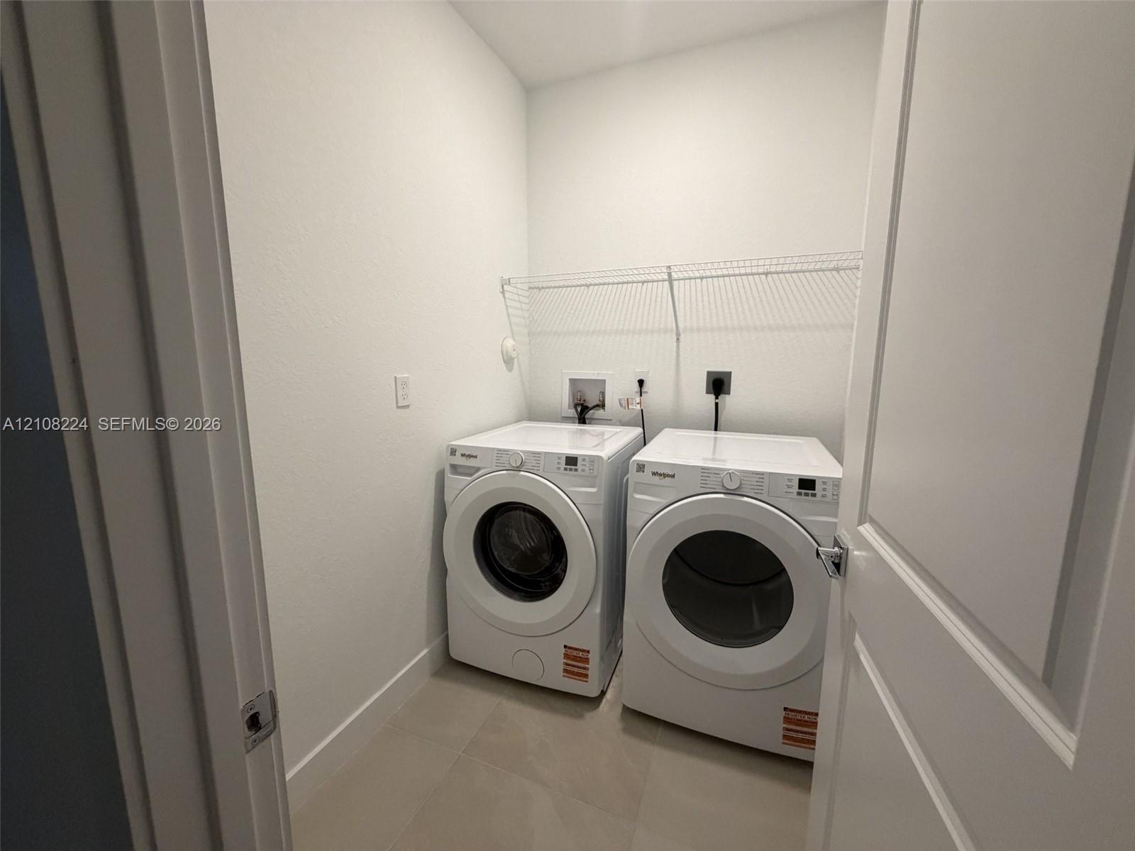 Utility room featuring neutral tile flooring, white interior walls, and wall-mounted wire shelving