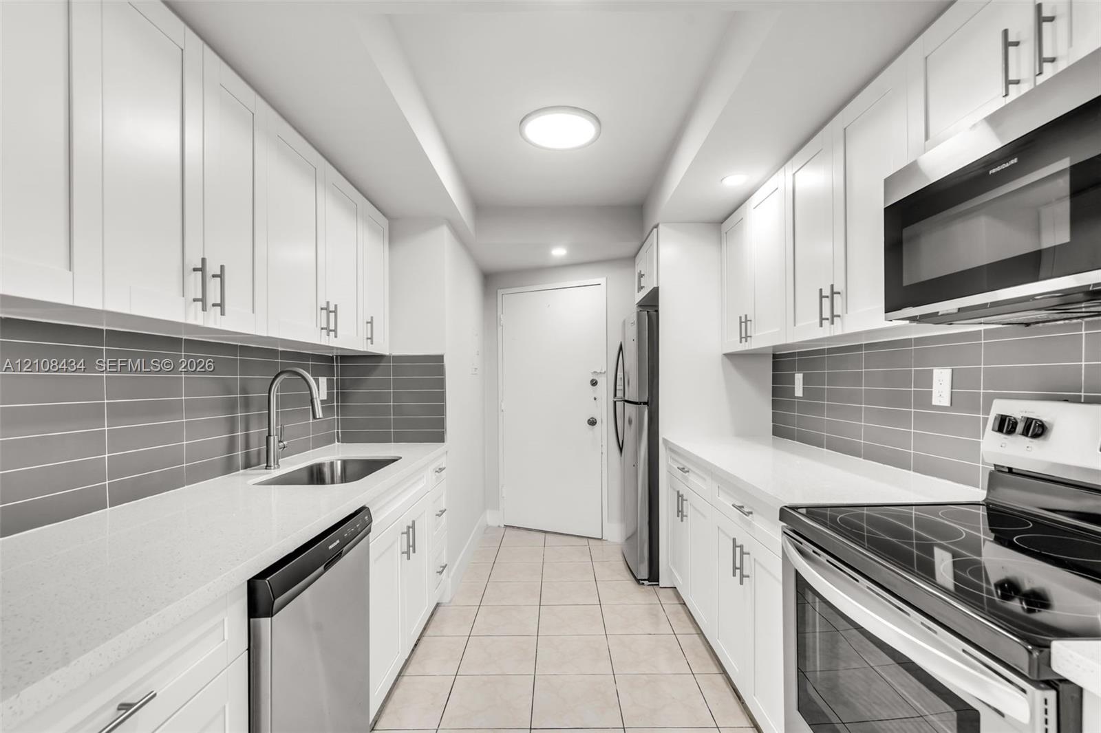Kitchen featuring white shaker-style cabinetry, white countertops, gray subway tile backsplash, stainless steel appliances, and tile flooring