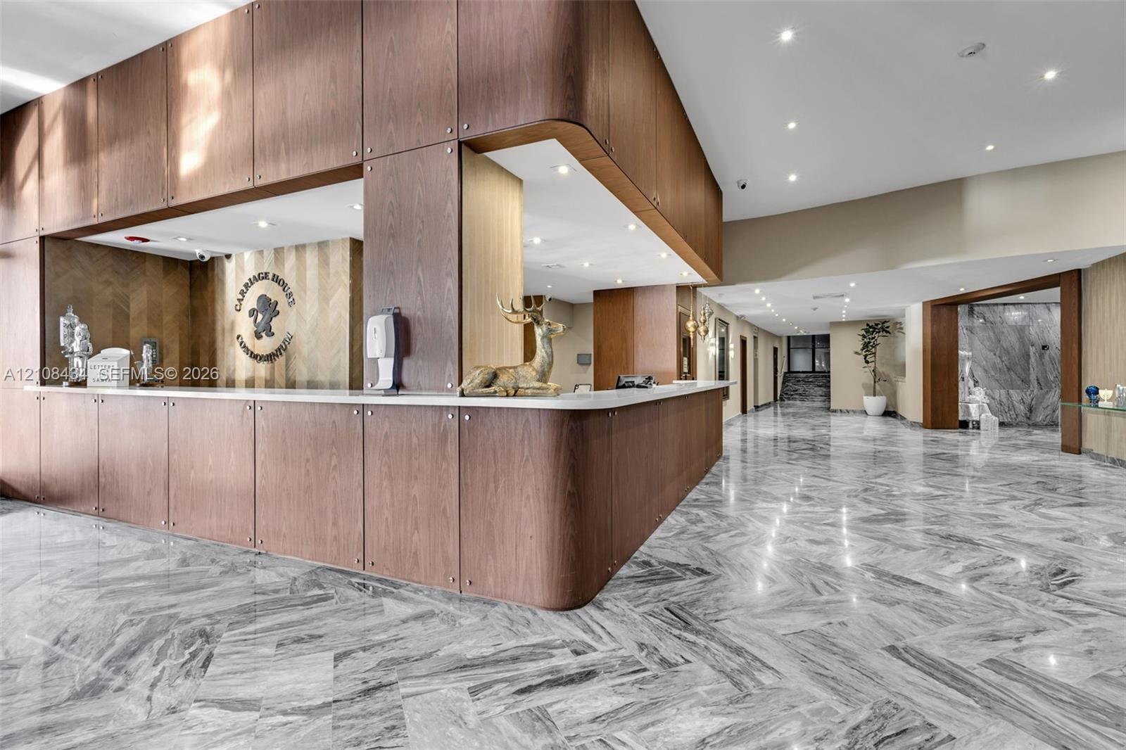 Lobby area featuring polished natural stone flooring in a herringbone pattern, wood-panelled custom reception desk with a solid surface countertop, an