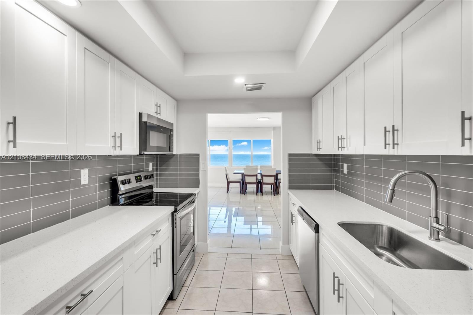 Kitchen featuring white shaker-style cabinetry, solid-surface countertops, horizontal gray tile backsplash, stainless steel appliances, and large-form