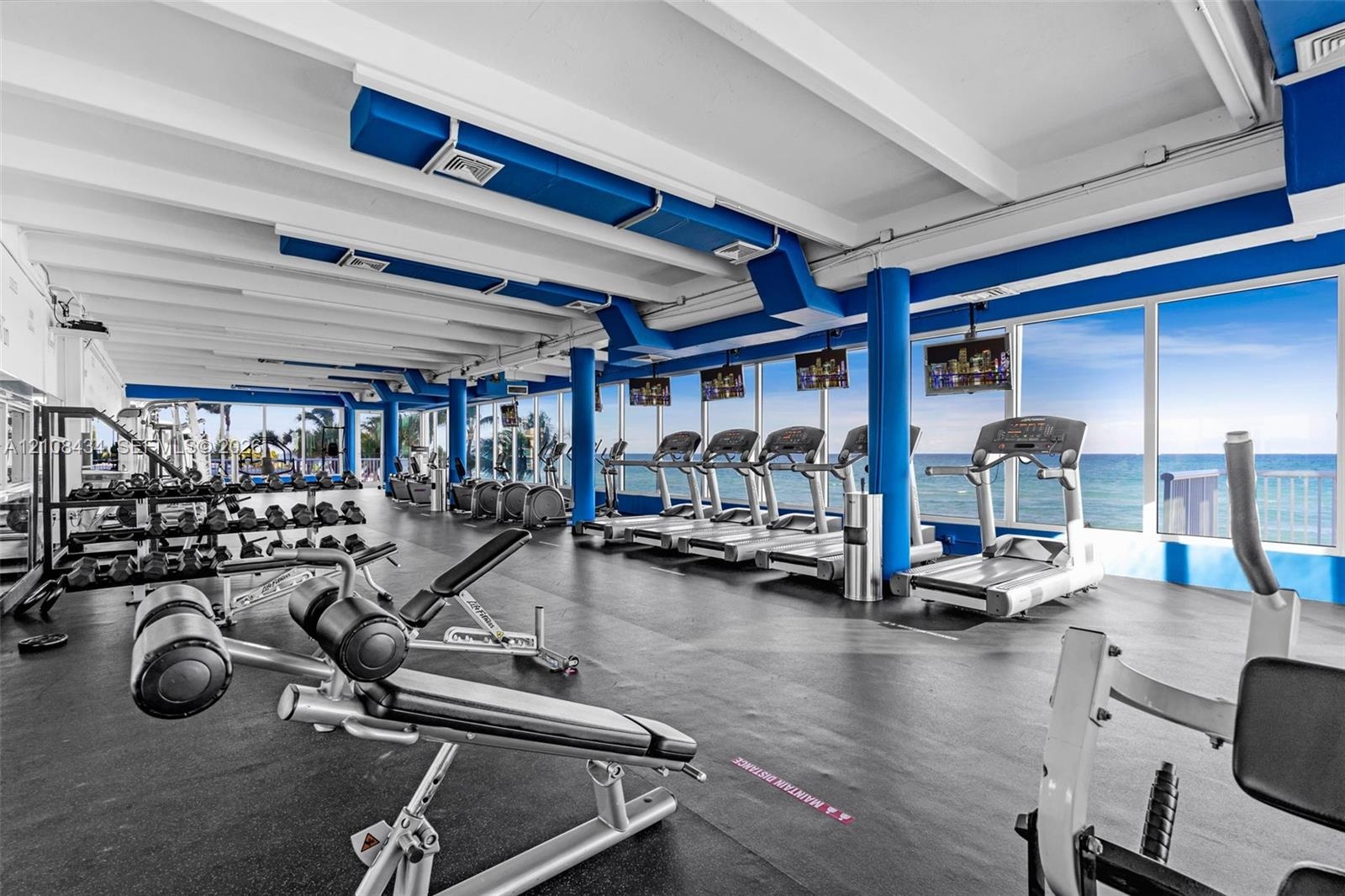 Fitness center featuring floor-to-ceiling windows with ocean scenery, exposed white beam ceilings, industrial-style exposed ductwork, and resilient ru