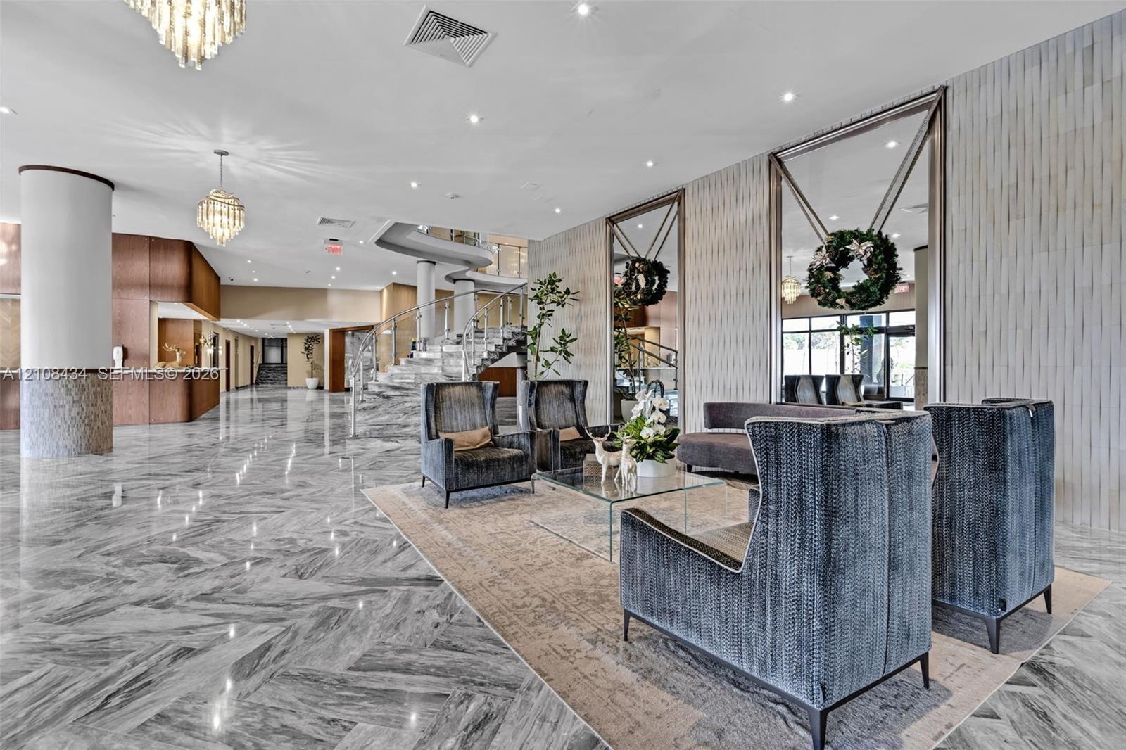 Expansive lobby featuring polished stone flooring in a herringbone pattern, floor-to-ceiling decorative mirrors, recessed lighting, crystal chandelier