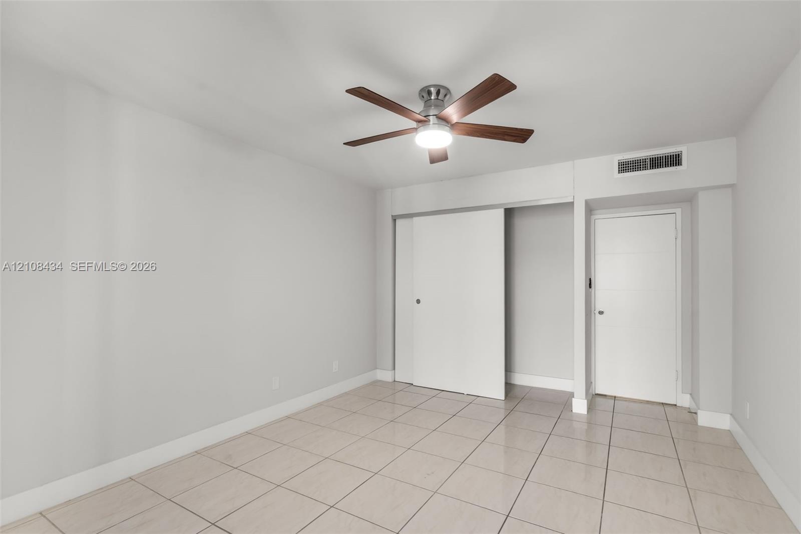 Neutral-toned room featuring large-format tile flooring, a multi-blade ceiling fan with integrated lighting, a sliding-door closet, and a contemporary
