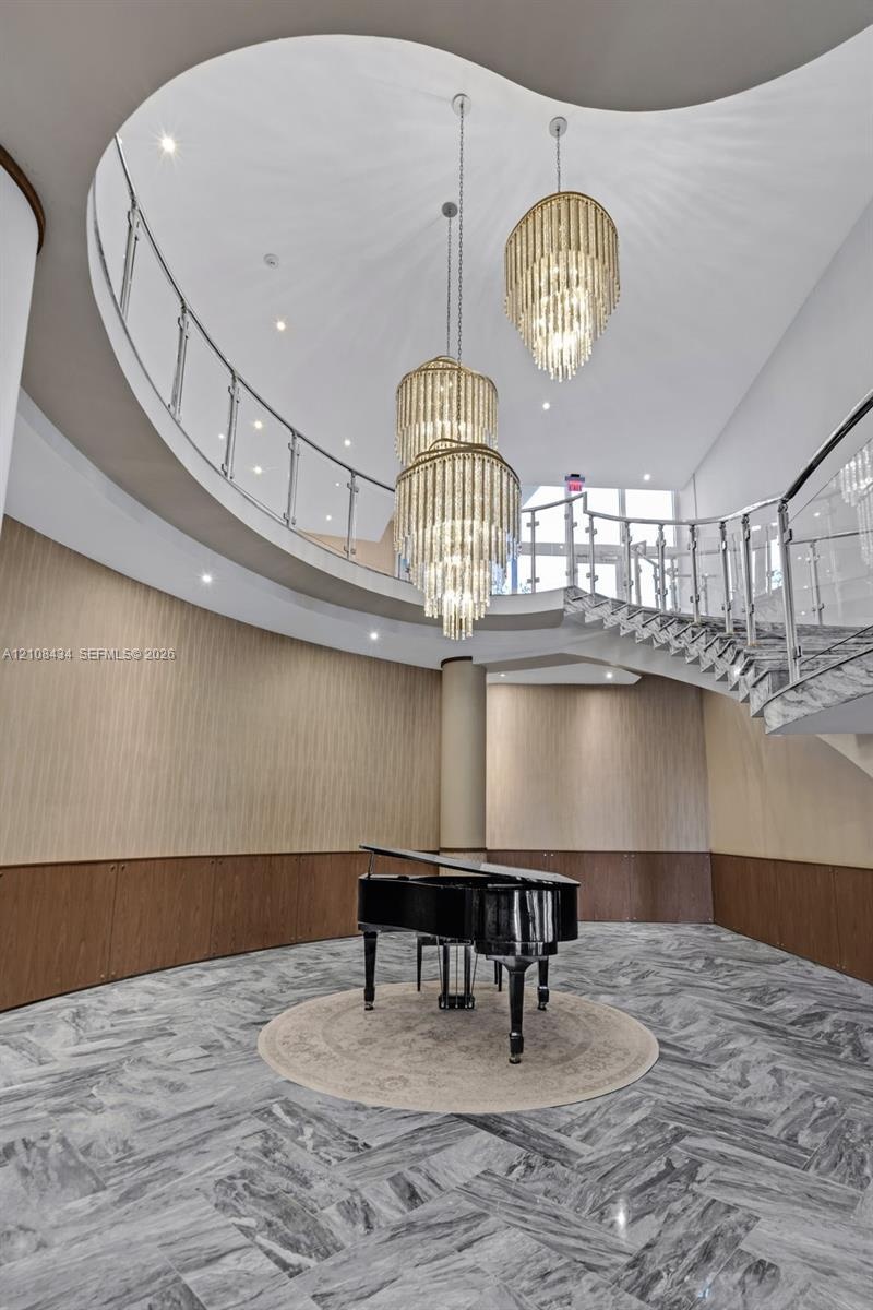 Grand foyer featuring a sweeping curved staircase with polished metal railings, tiered crystal chandeliers, stone flooring in a herringbone pattern, a