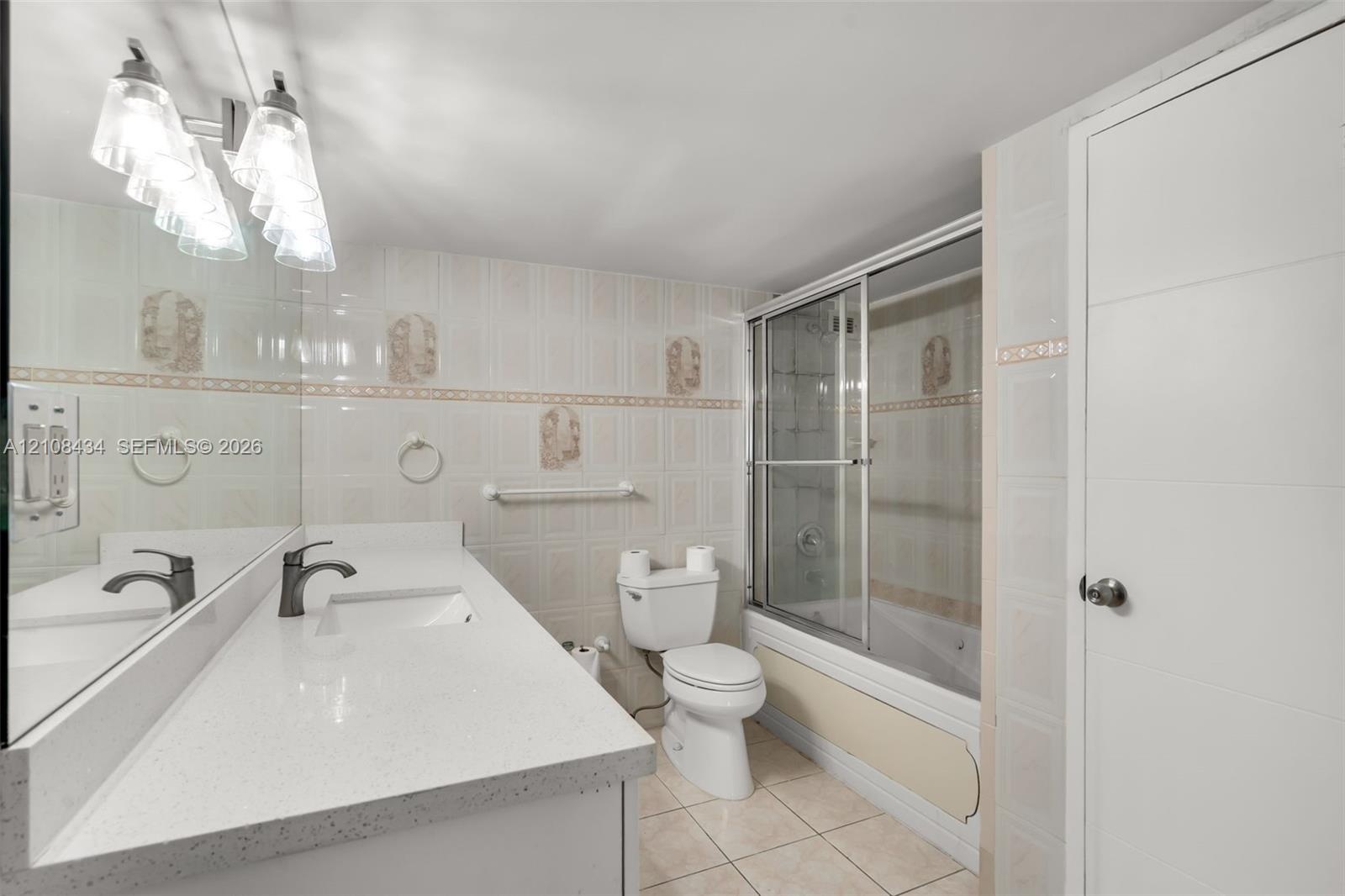 Bathroom featuring a quartz-topped vanity with an integrated basin, ceramic tile flooring, full-width wall mirror, and a tub-shower combination enclos
