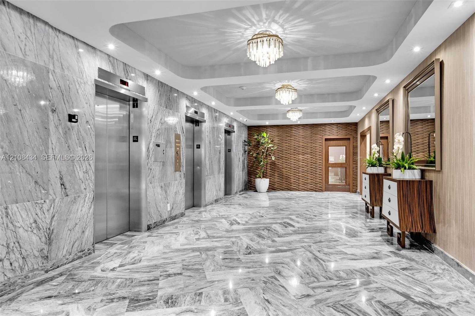 Polished stone flooring in a herringbone pattern, full-height stone wall cladding, stainless steel elevator doors, recessed tray ceiling with multi-ti