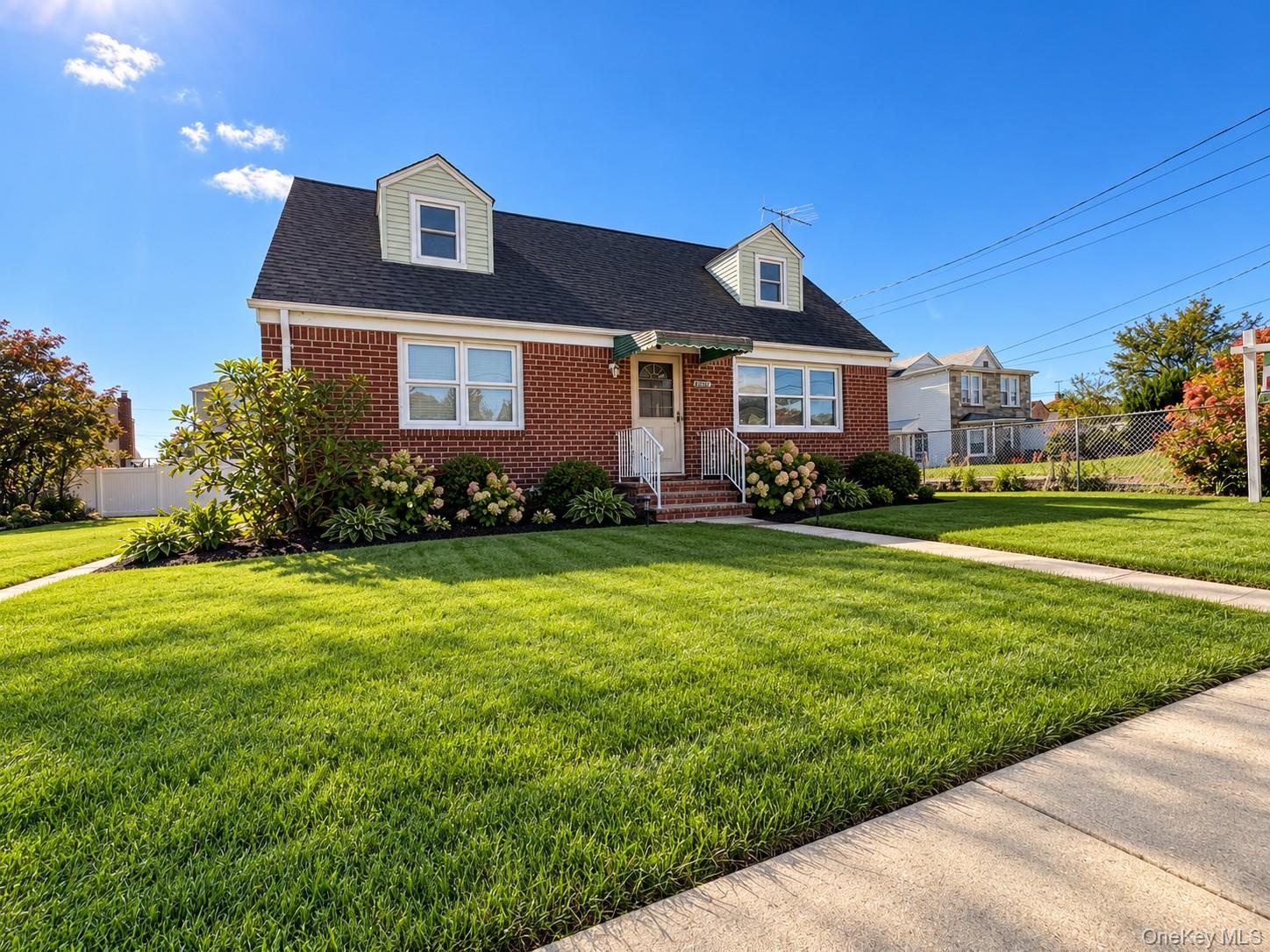 Brick exterior featuring dual front-facing dormers, a shingled roof, a covered entryway, and manicured landscaping