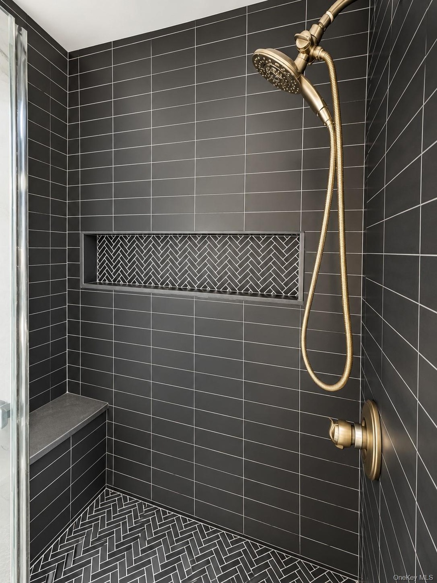 Shower stall featuring matte black subway wall tile, herringbone-patterned floor and niche tile, integrated stone-finish bench, and brass-finish fixtu