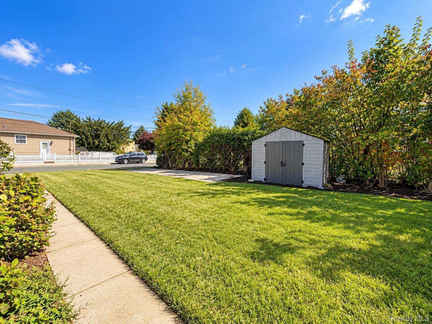 Expansive backyard featuring a level lawn, concrete walkway, detached storage shed, and mature perimeter landscaping