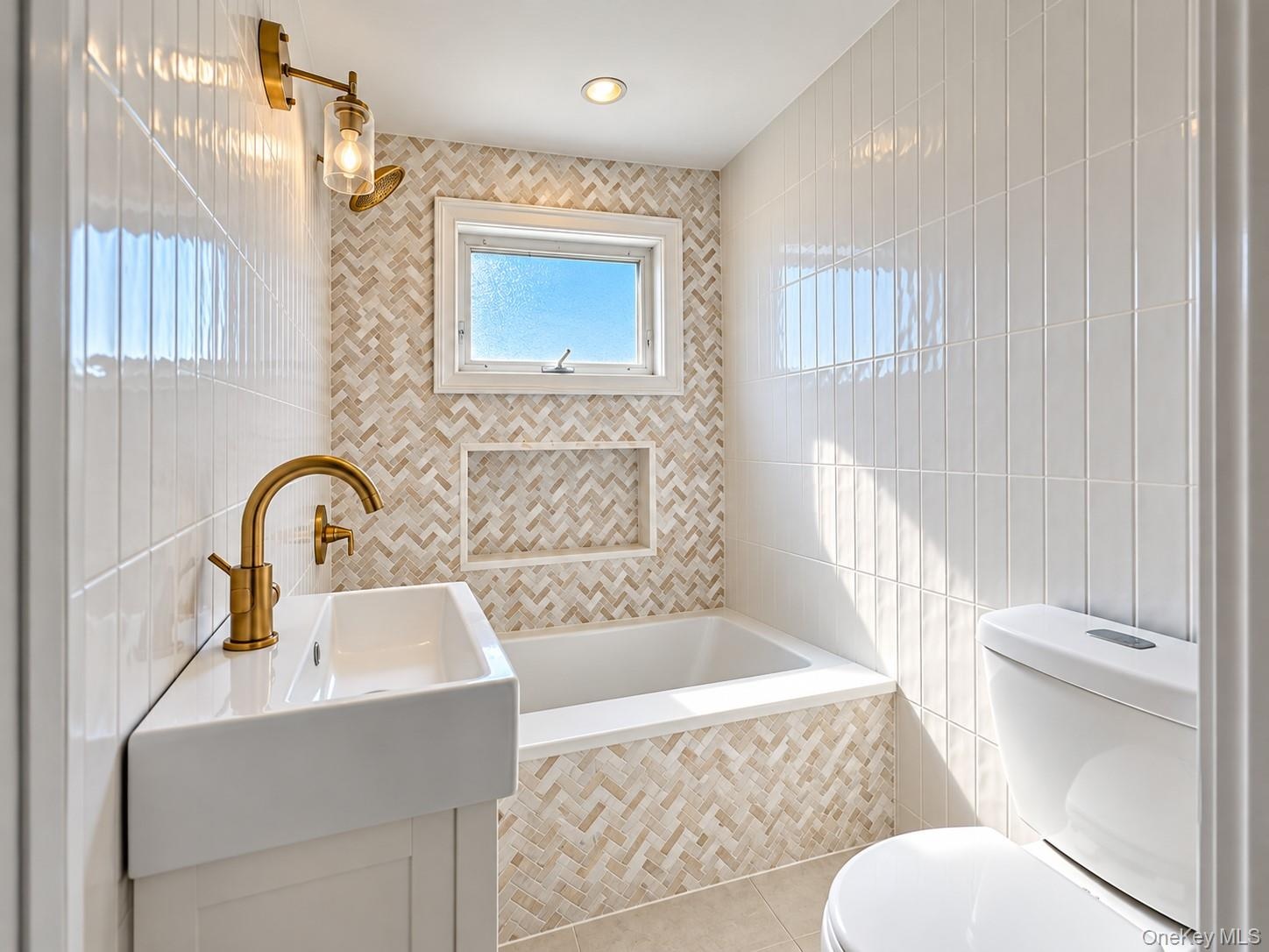 Full bathroom featuring herringbone-patterned stone tile accents, a recessed wall niche, a deep soaking tub with a surrounding tiled deck, and a moder