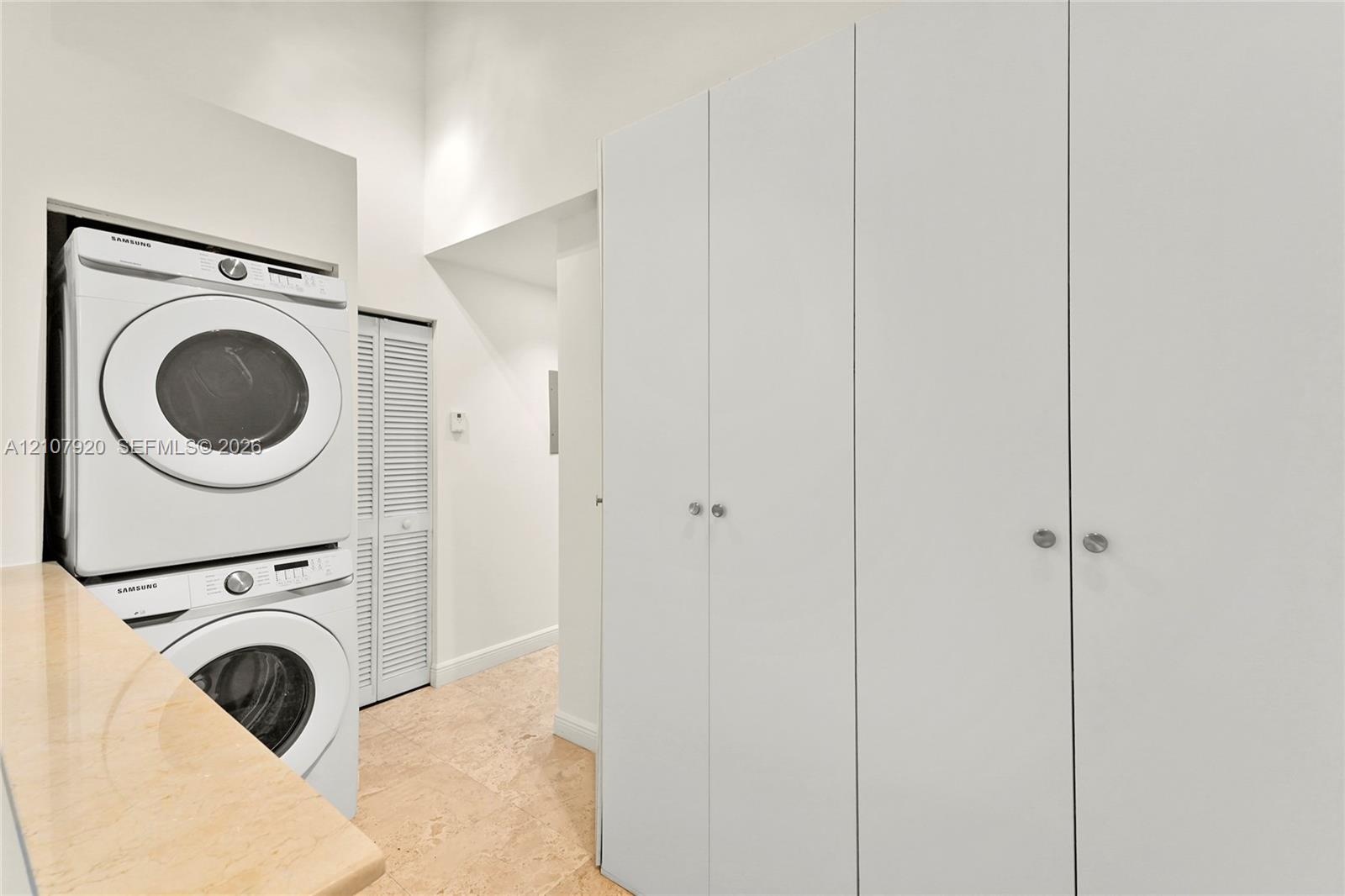 Laundry area featuring floor-to-ceiling built-in cabinetry, stacked appliances, stone-surface countertop, and louvered closet doors