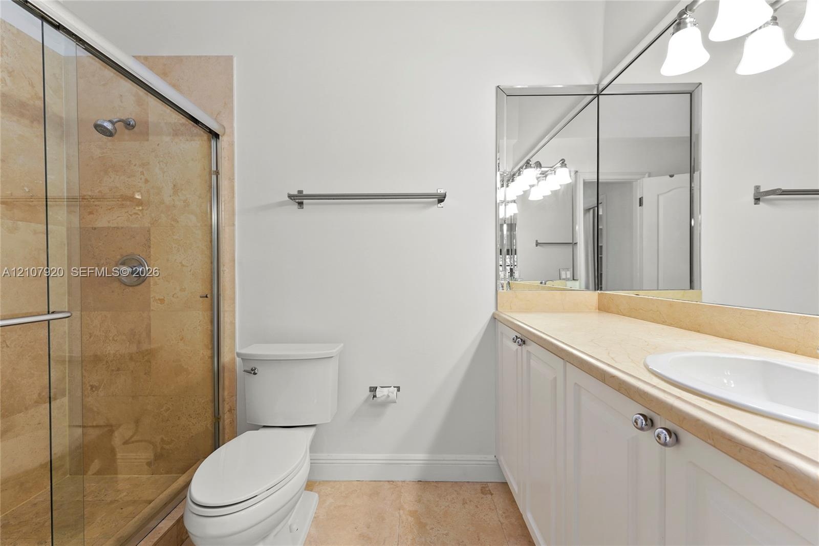 Walk-in shower with stone tile surround, vanity with stone countertop, integrated undermount sink, expansive vanity mirror, and polished metal fixture