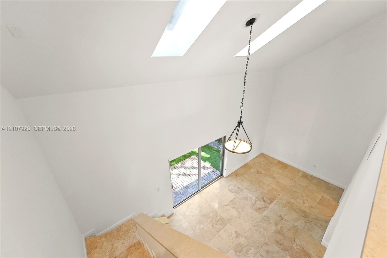 Vaulted ceiling featuring dual skylights, stone tile flooring, and a suspended chandelier, with sliding glass doors opening to a paved exterior space