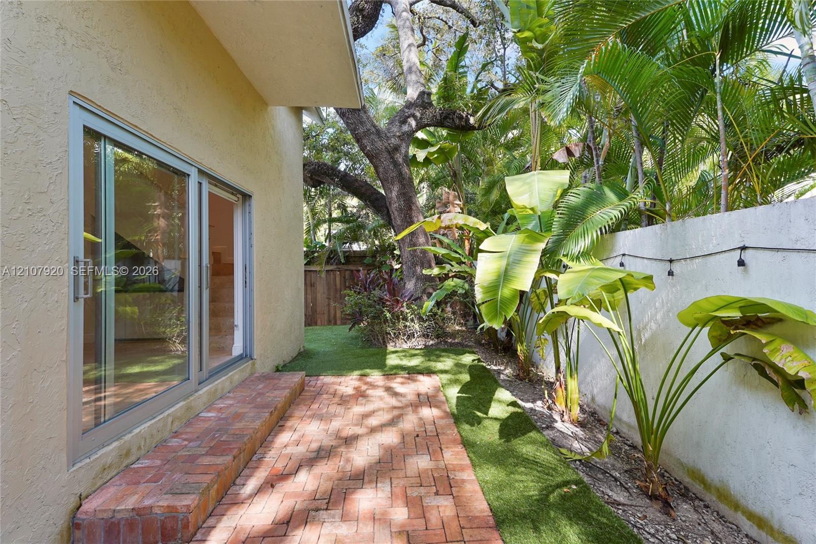 Exterior patio featuring red brick paving, sliding glass doors, synthetic turf landscaping, and a concrete masonry wall