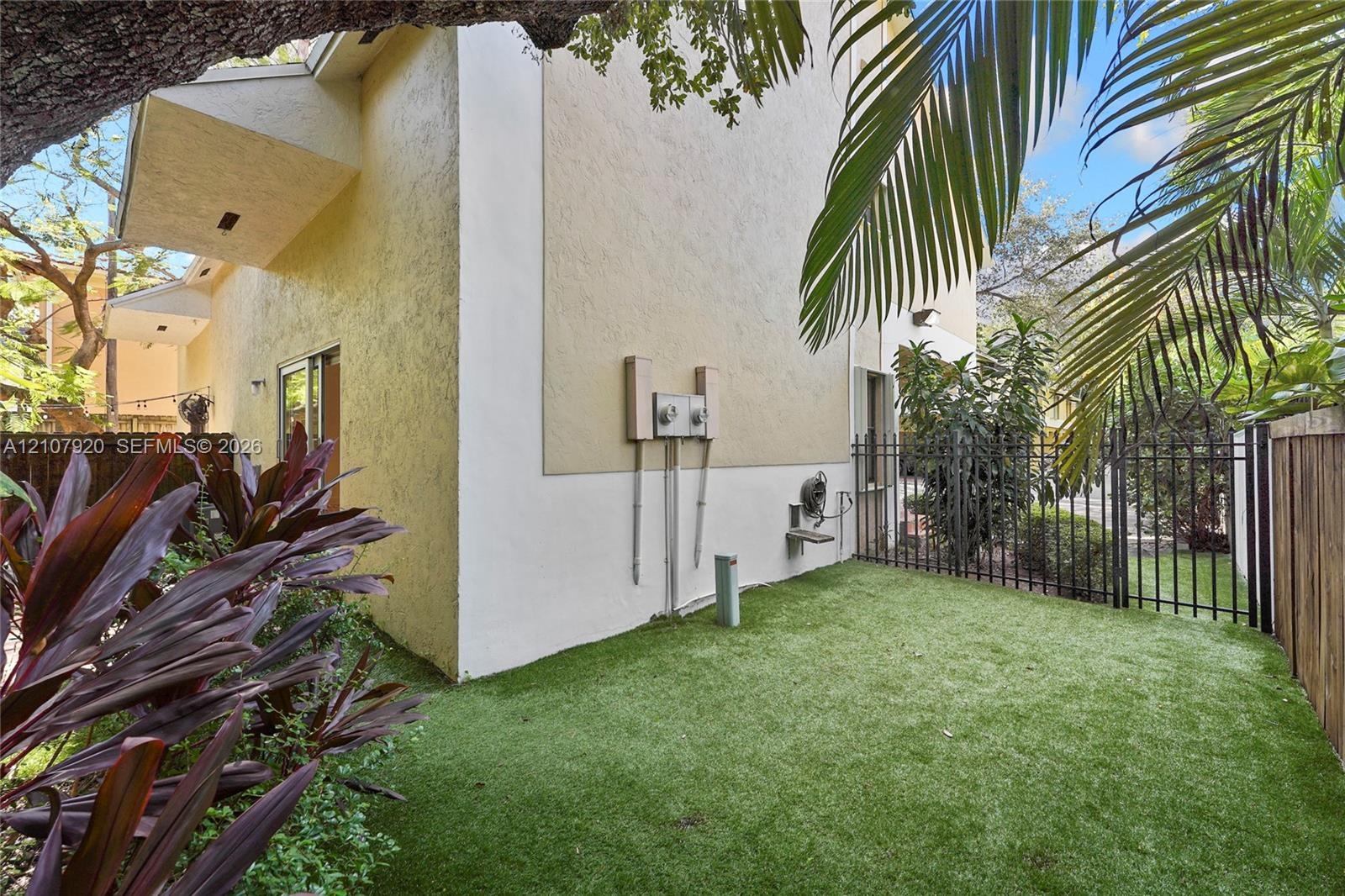 Stucco exterior, fenced yard with synthetic turf, mature landscaping, and sliding glass door entry