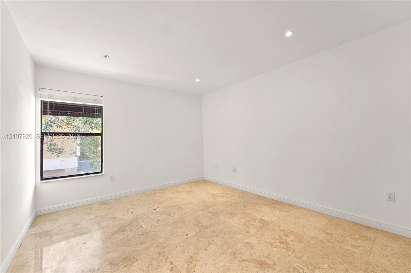 Bright corner room featuring abundant natural light from a large multi-pane window, recessed ceiling lighting, smooth drywall finishes, and light wood