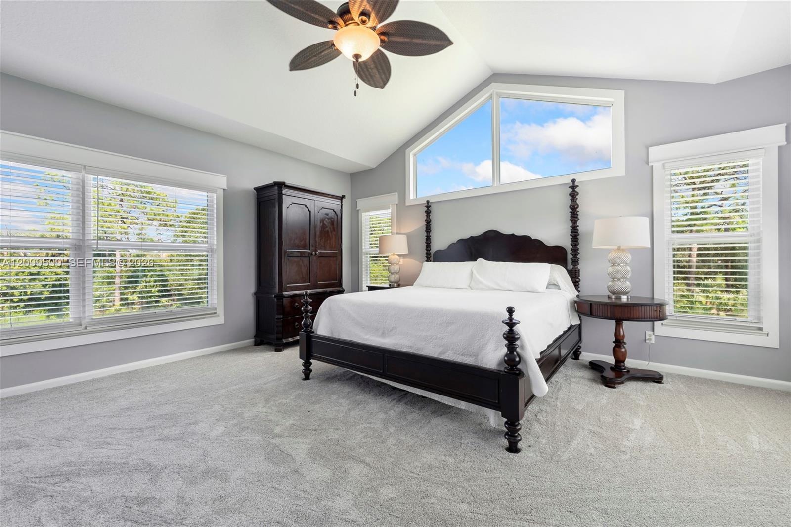 Vaulted ceiling featuring a ceiling fan, neutral carpeting, and oversized windows including a geometric transom window