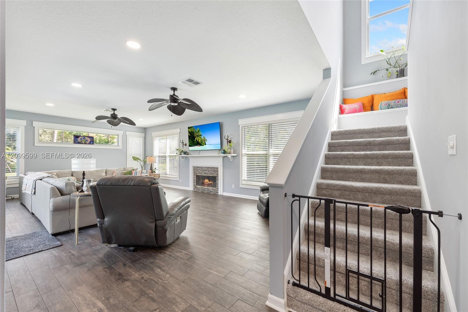 Open-concept interior featuring wood-finish flooring, recessed lighting, multiple ceiling fans, a tile-surround fireplace with a mantel, and carpeted 
