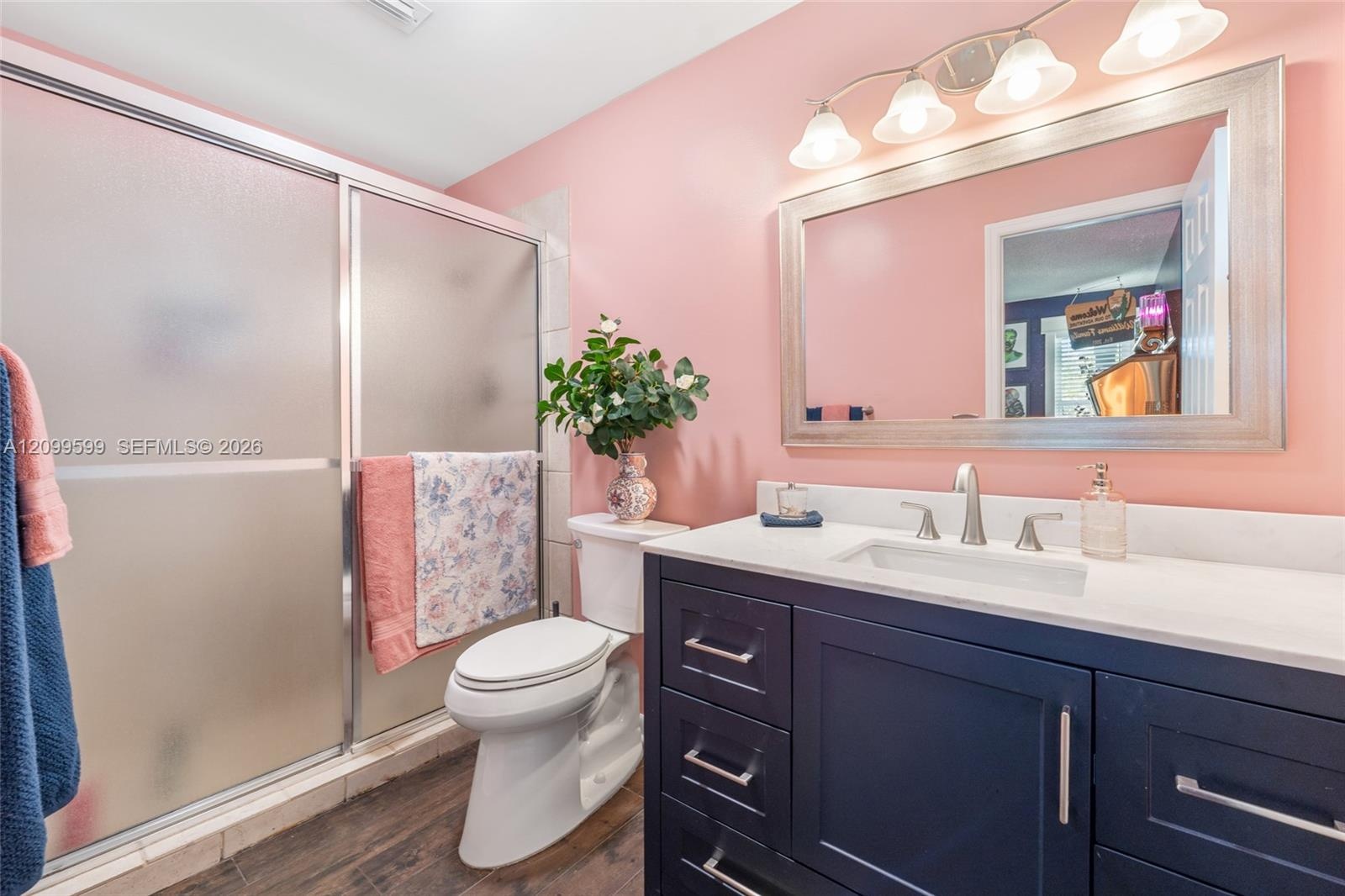 Dark navy shaker-style vanity with a light-toned countertop, undermount sink, brushed nickel hardware, and a glass-enclosed shower featuring a framed 
