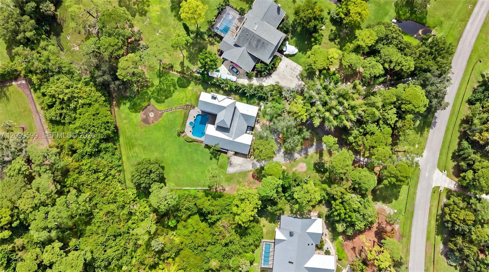 Aerial perspective of residential property featuring a metal roof, private swimming pool, concrete driveway, stone walkway, and expansive mature lands