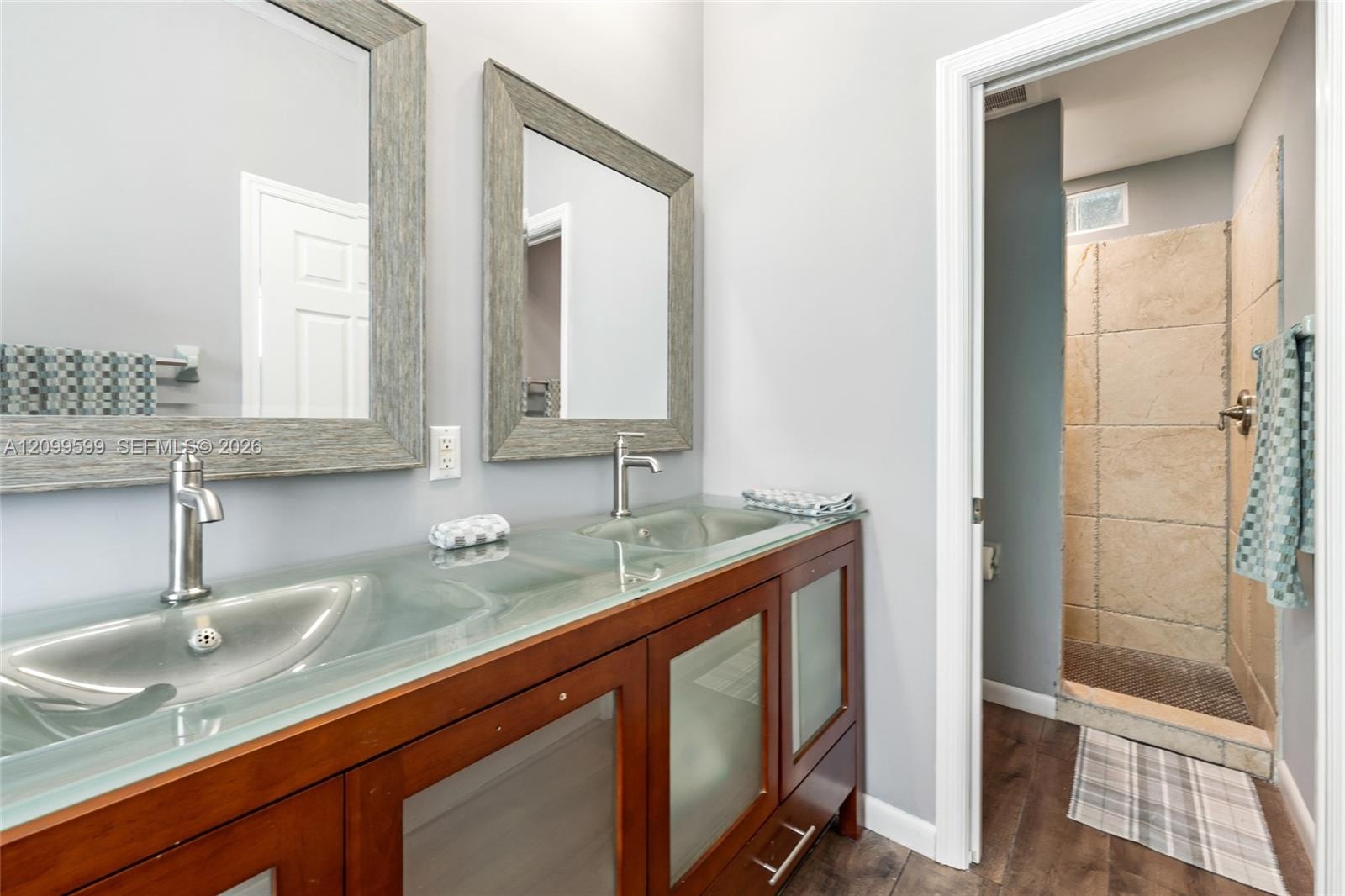 Double vanity featuring a translucent glass countertop with integrated dual basins, wooden cabinetry with frosted glass panels, two framed mirrors, an