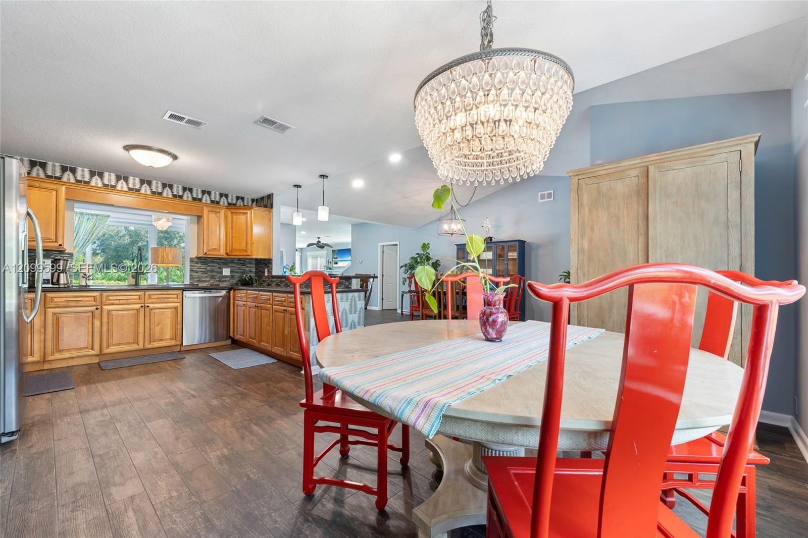 Kitchen featuring wood-finish cabinetry, stone-texture backsplash, stainless steel appliances, wood-finish flooring, and a tiered crystal chandelier