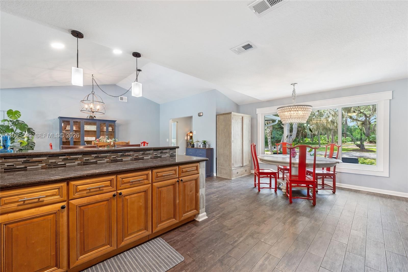 Kitchen featuring wood cabinetry, stone-finish countertops with a mosaic tile backsplash, wood-finish flooring, vaulted ceilings, and large windows wi