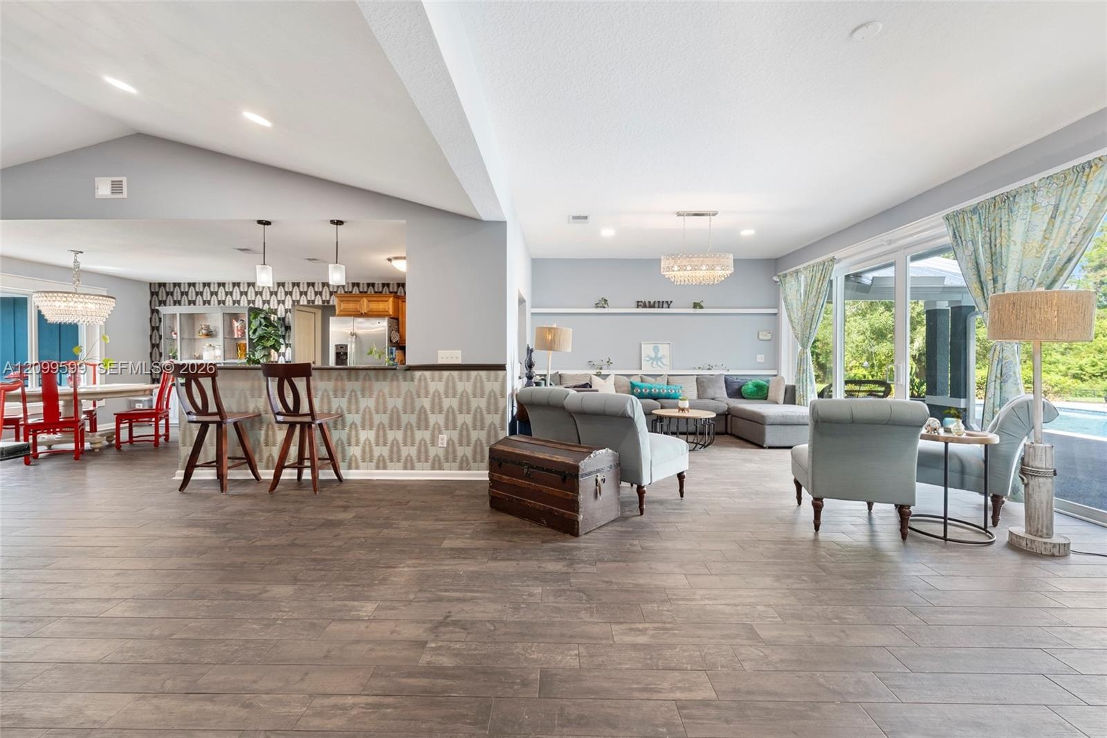 Open-concept interior featuring wood-finish tile flooring, vaulted ceilings, built-in shelving, glass sliding doors, and a decorative breakfast bar