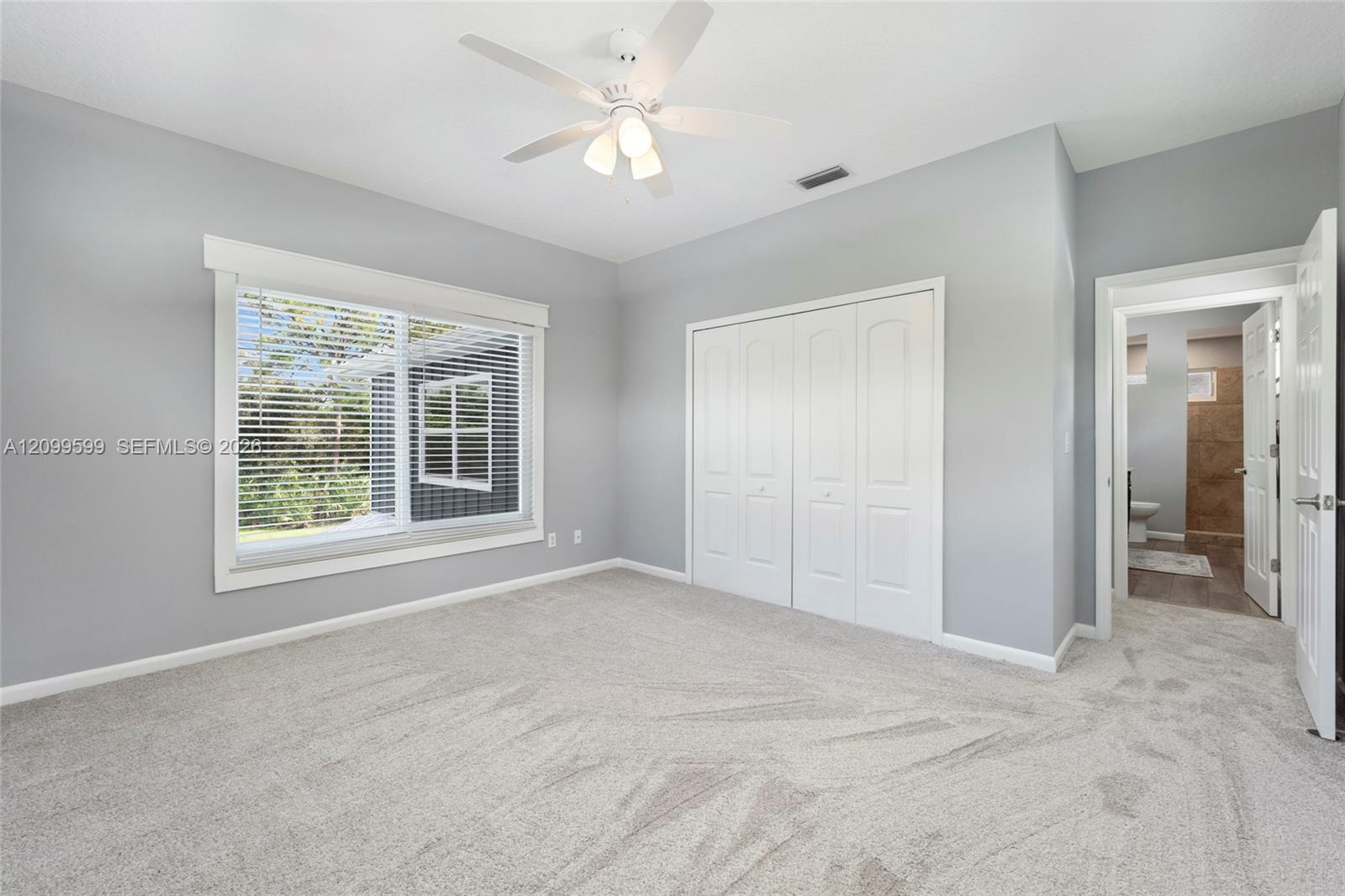 Neutral wall color, carpeted flooring, large window with blinds, bi-fold closet doors, and a ceiling fan with integrated lighting