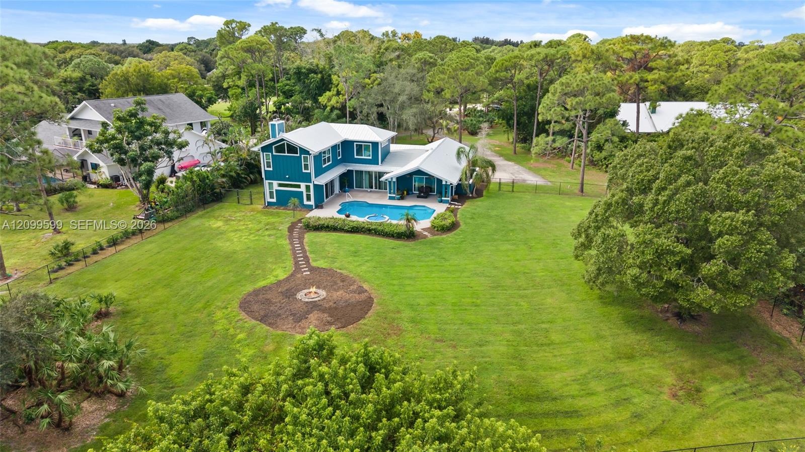 Aerial perspective of a multi-level residence featuring a metal roof, an in-ground swimming pool with a stone paver deck, a circular stone fire pit, a